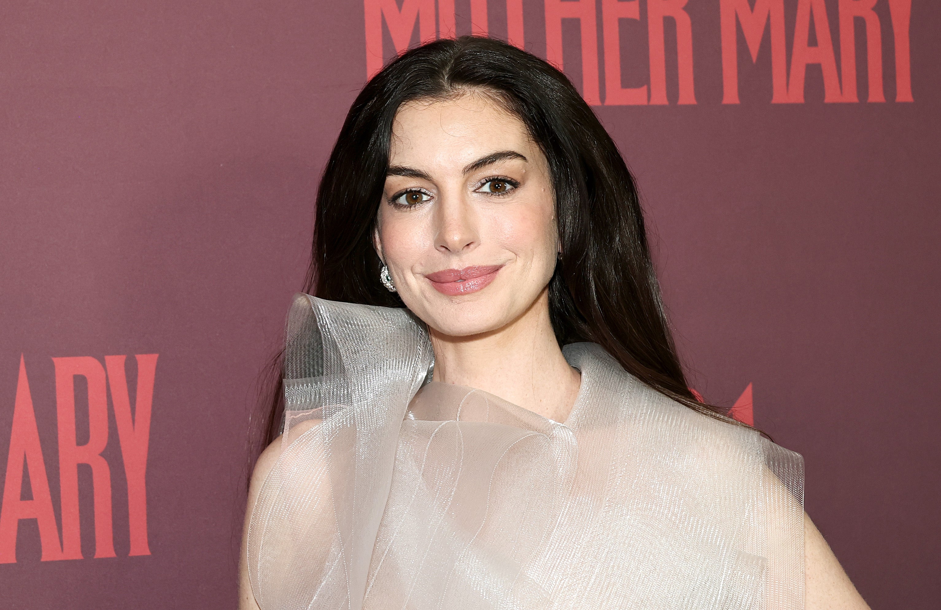 Woman connected reddish carpet successful sheer, structured formal with bold enarthrosis detail, against backdrop with "Mother Mary" text