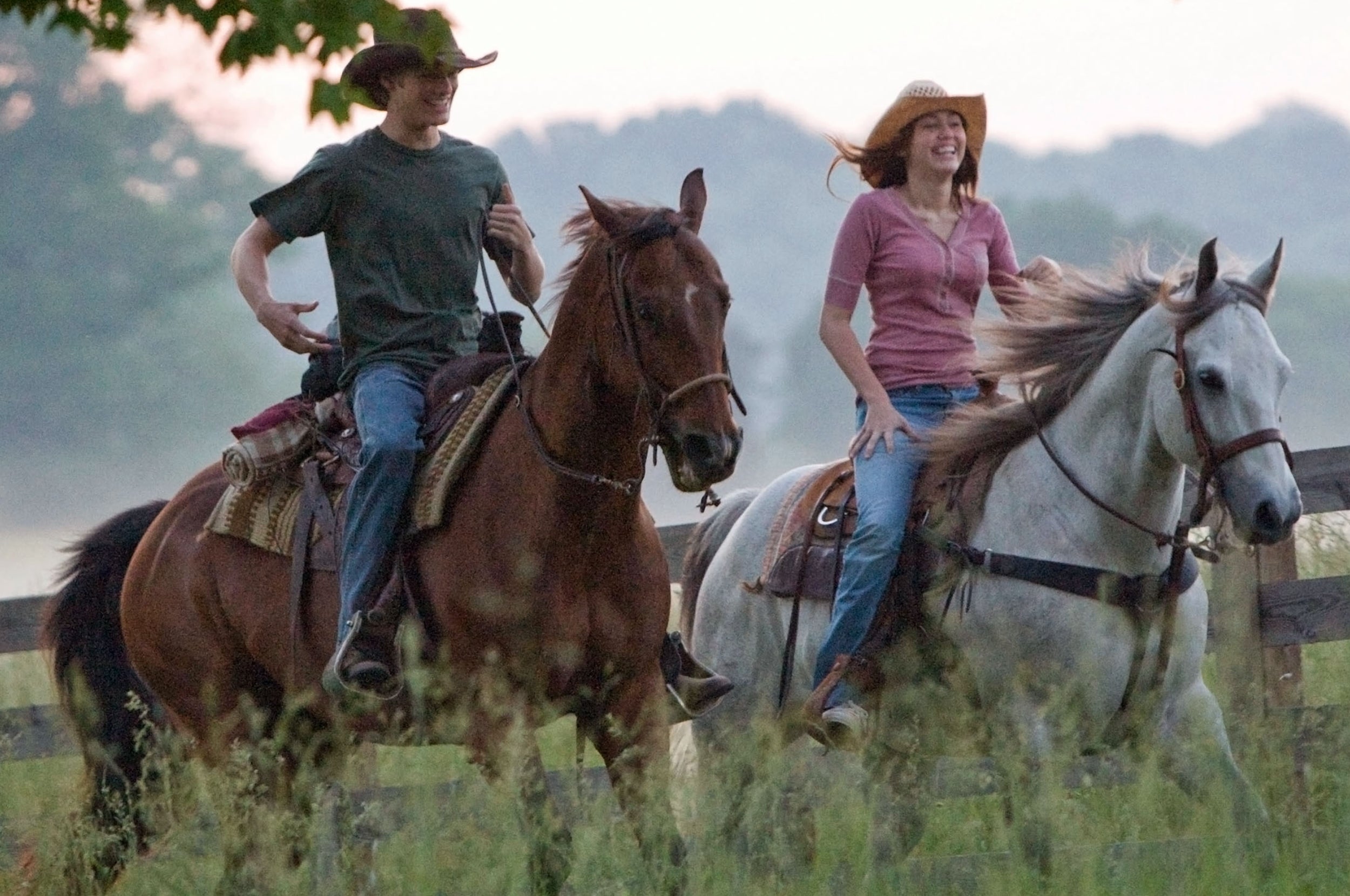 Two people wearing hats ride horses on a grassy path, enjoying a leisurely outdoor activity