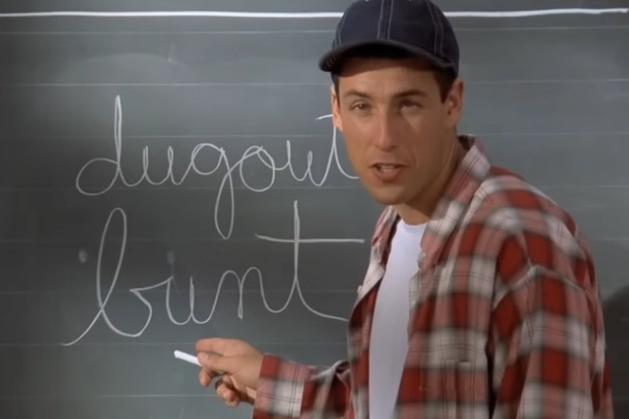 Adam Sandler in "Billy Madison" wearing a baseball cap and flannel shirt stands in front of a chalkboard with the words "dugout" and "bunt" written on it