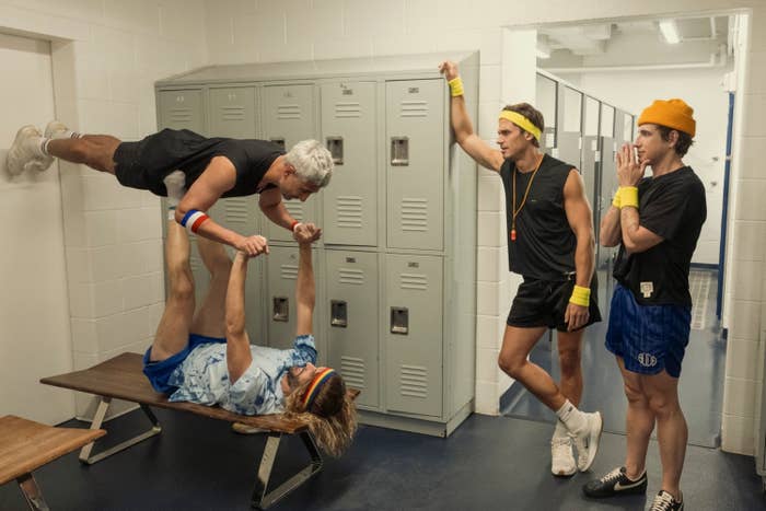 People dressed successful  retro gym attire, performing a radical  stunt successful  a locker room, with 1  idiosyncratic   elevated horizontally supra  different  connected  a bench