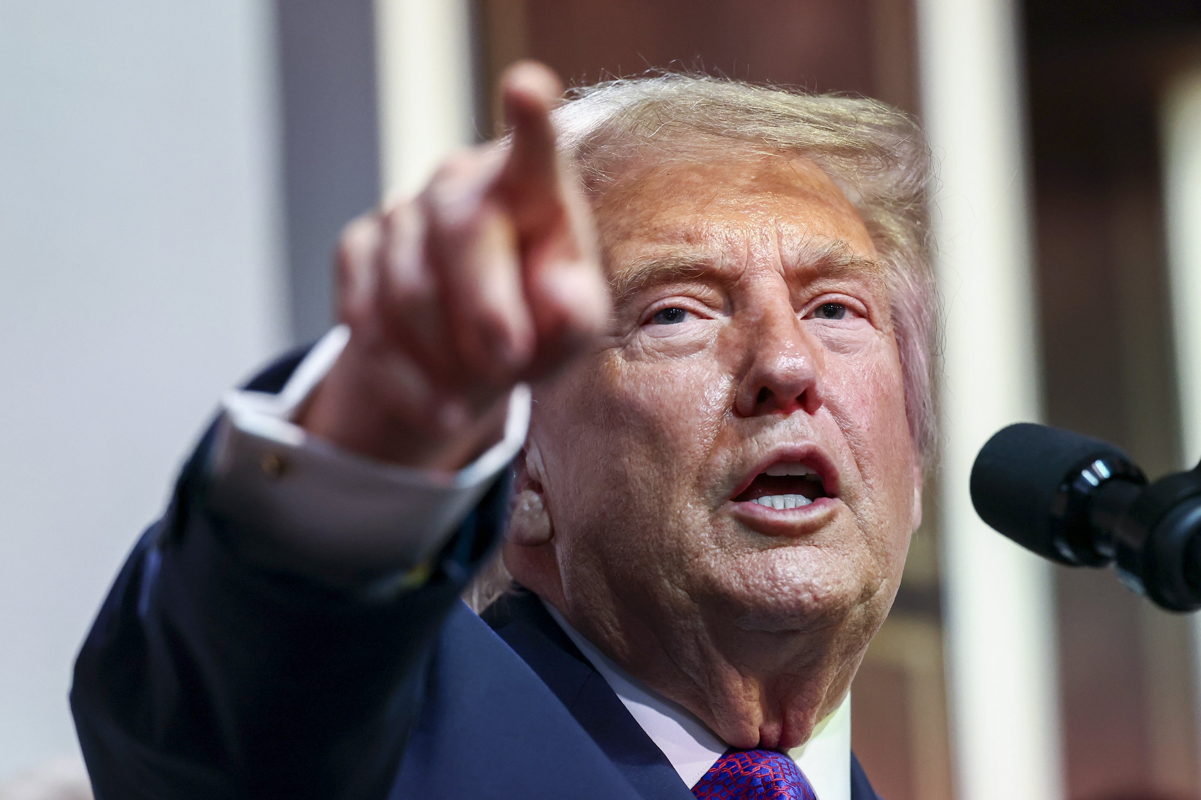 Person speaking at a microphone, pointing toward the camera, appearing to be engaged in a speech or public address