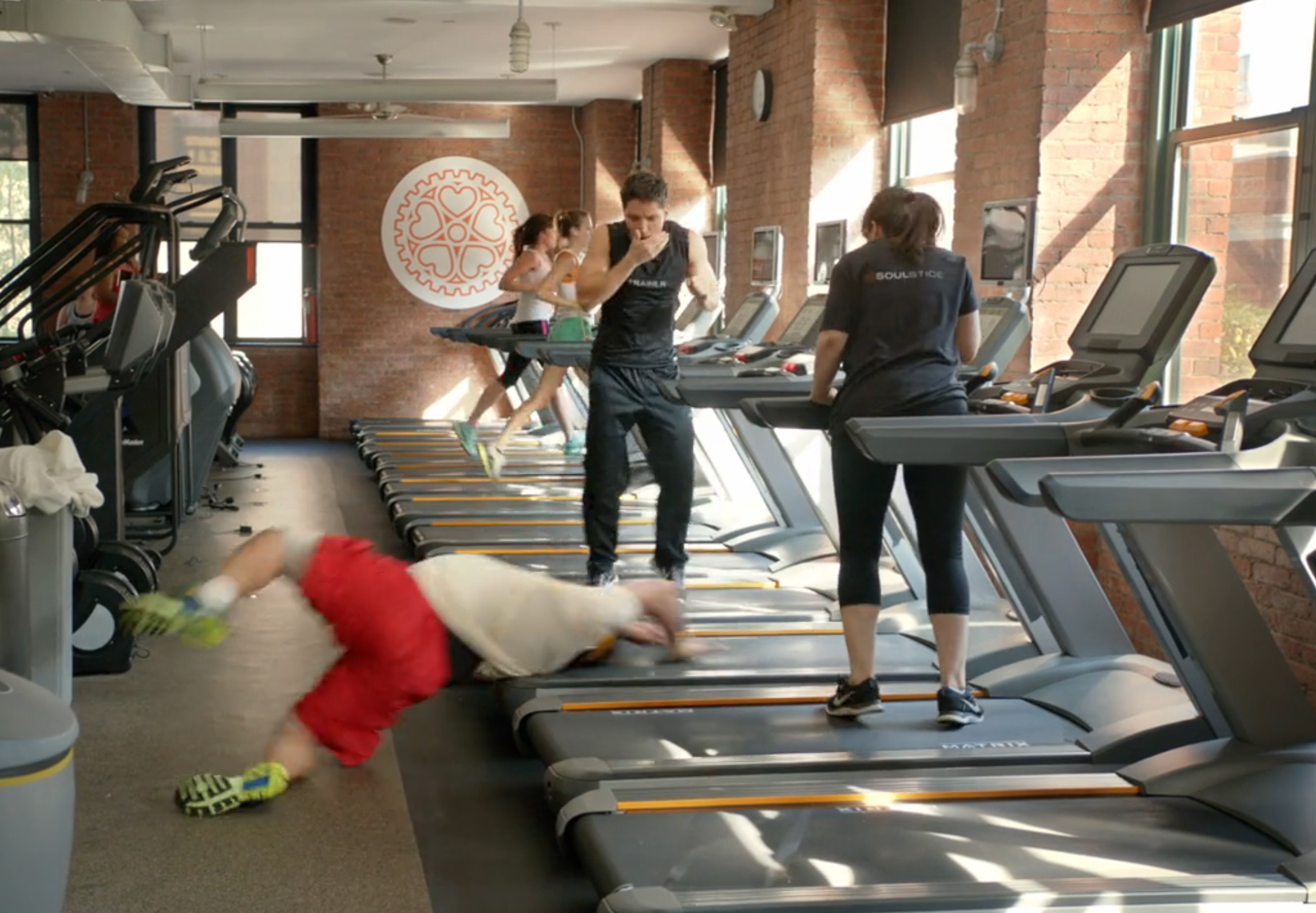 Person falling disconnected a treadmill successful a gym, portion others absorption connected their workouts. Exercise instrumentality and fittingness activities visible