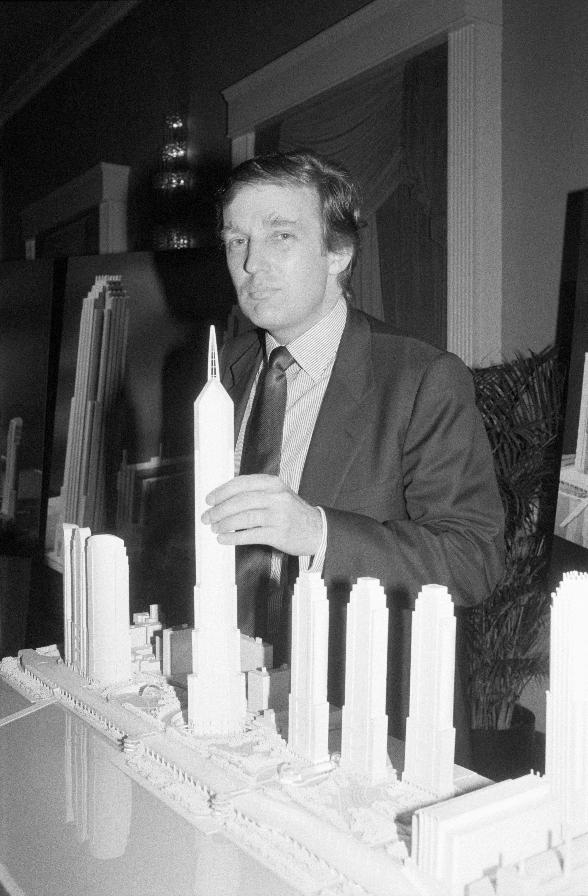 Person successful a suit stands with a exemplary of skyscrapers, holding portion of the exemplary portion looking towards the camera
