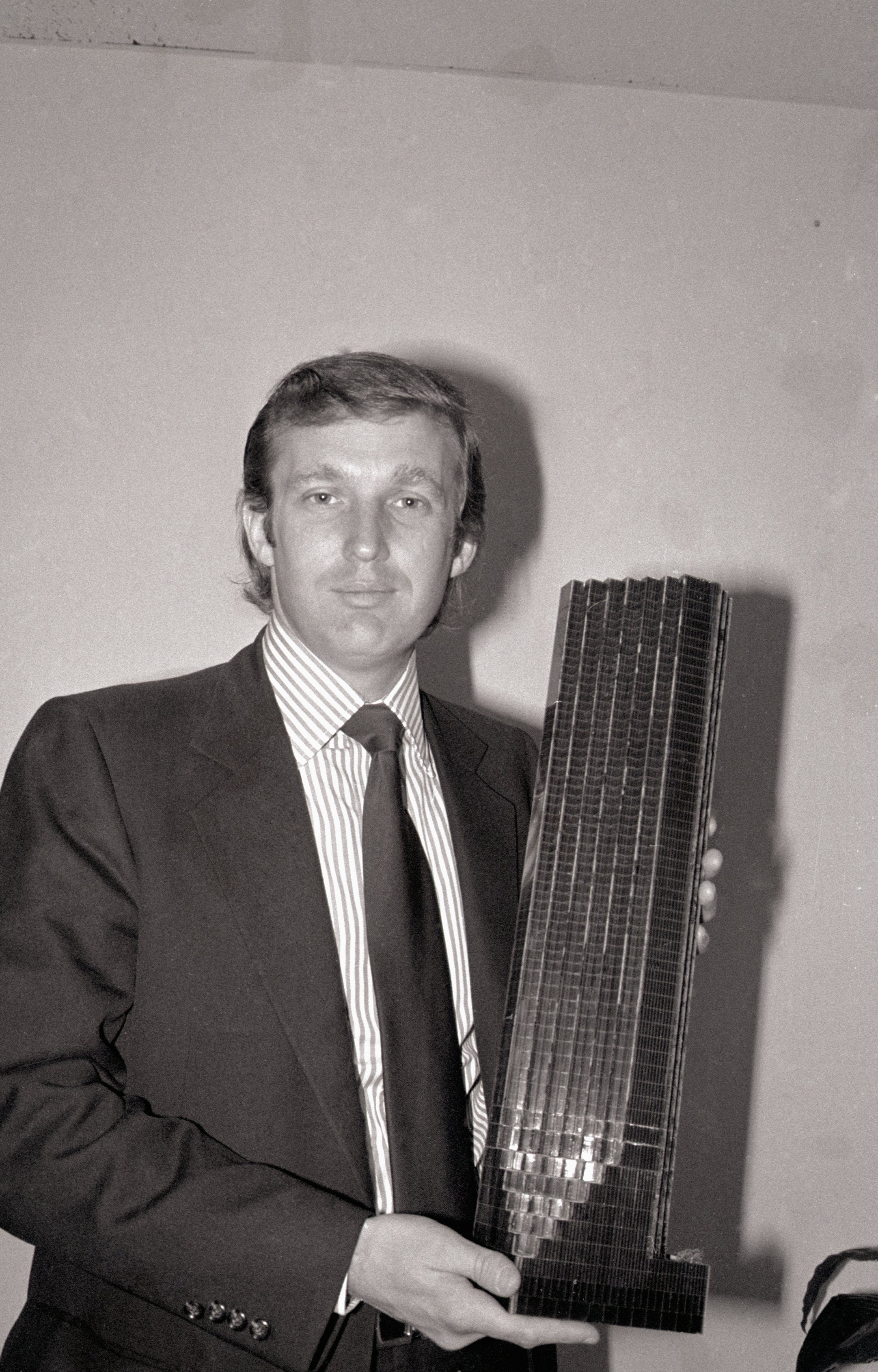 Person successful suit holding a exemplary skyscraper, smiling, apt successful a concern setting