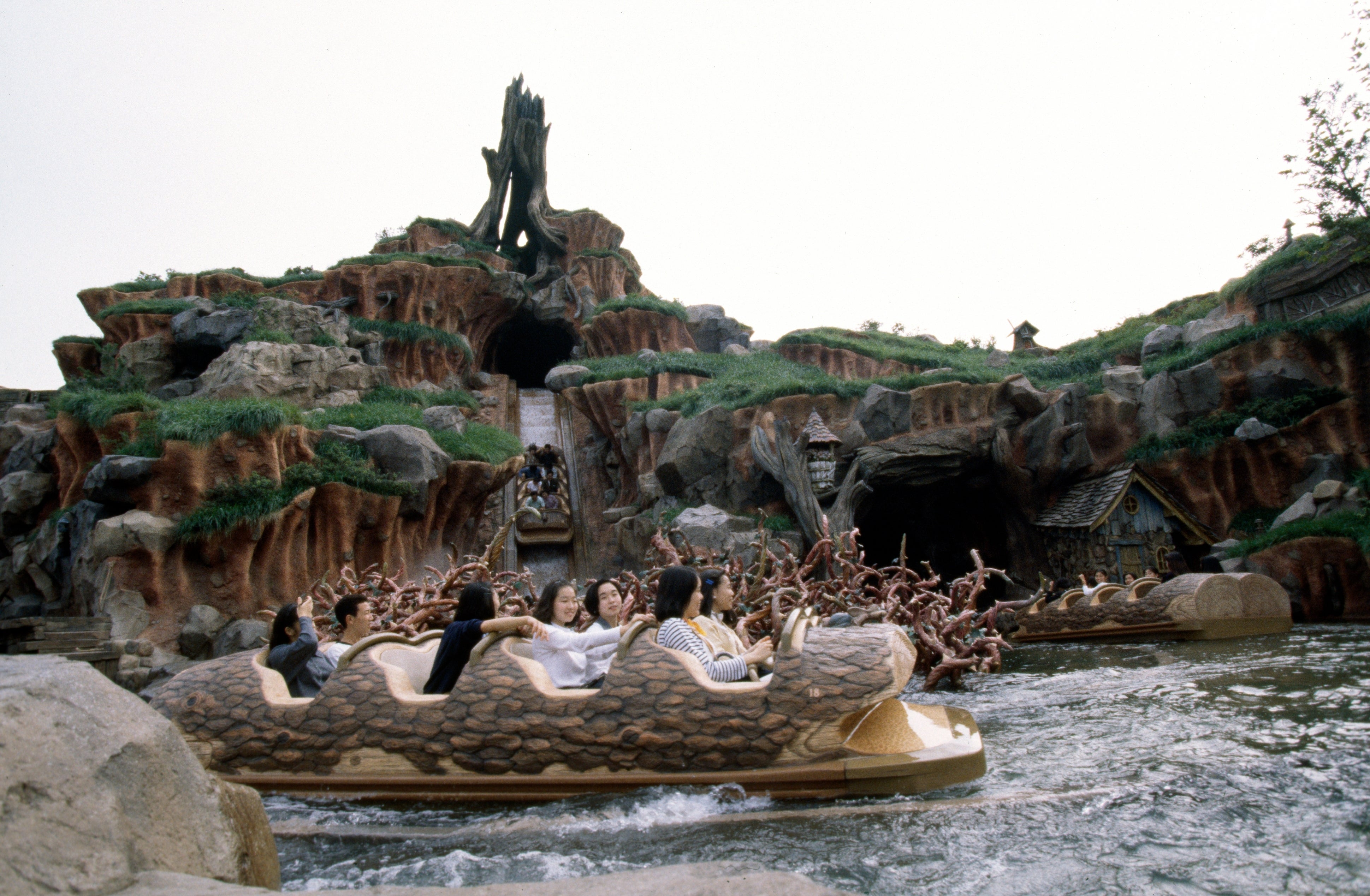 People enjoying a log flume ride at a theme park, surrounded by rocky terrain and a waterfall in the background