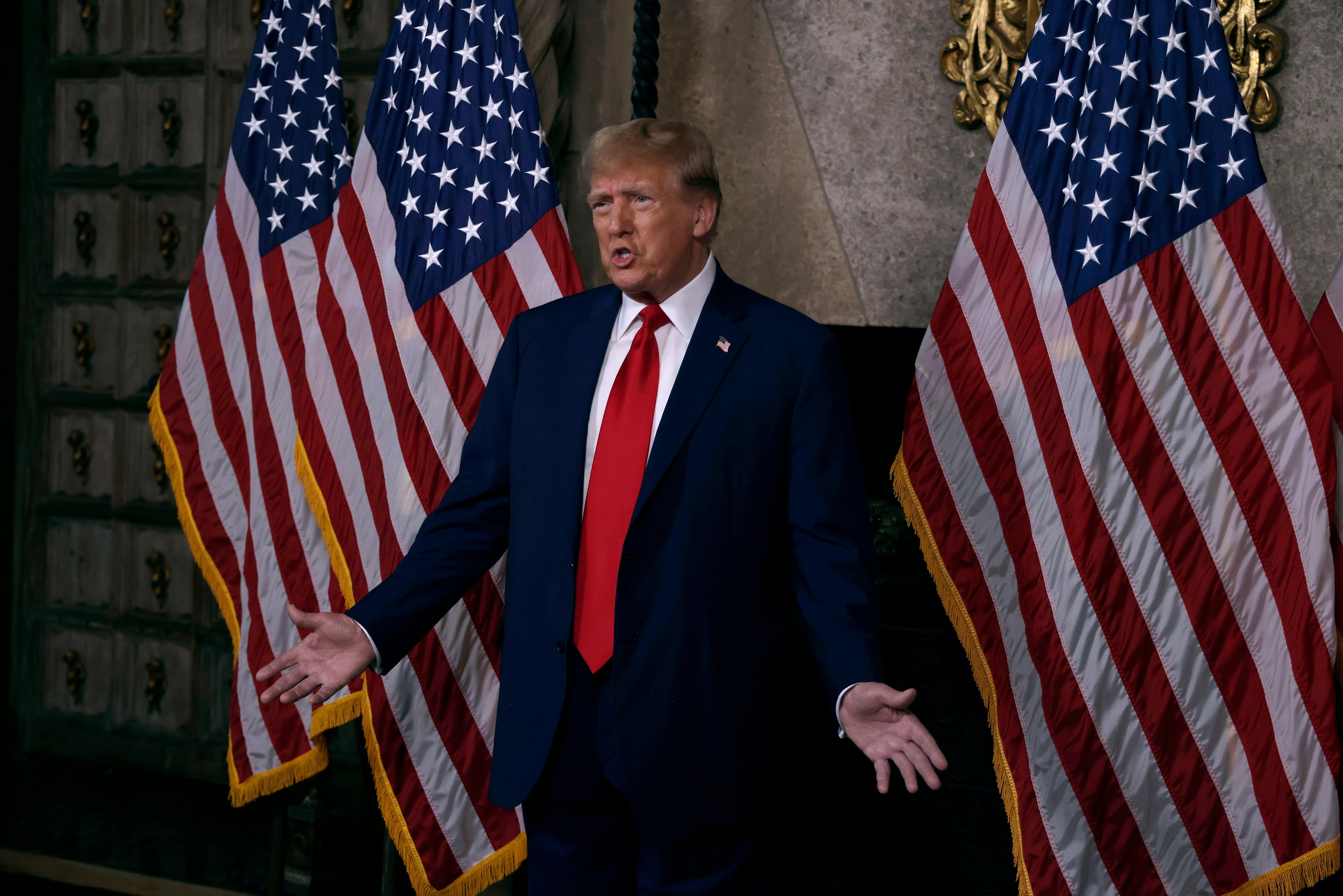 A idiosyncratic successful a suit stands with arms unfastened successful beforehand of U.S. flags