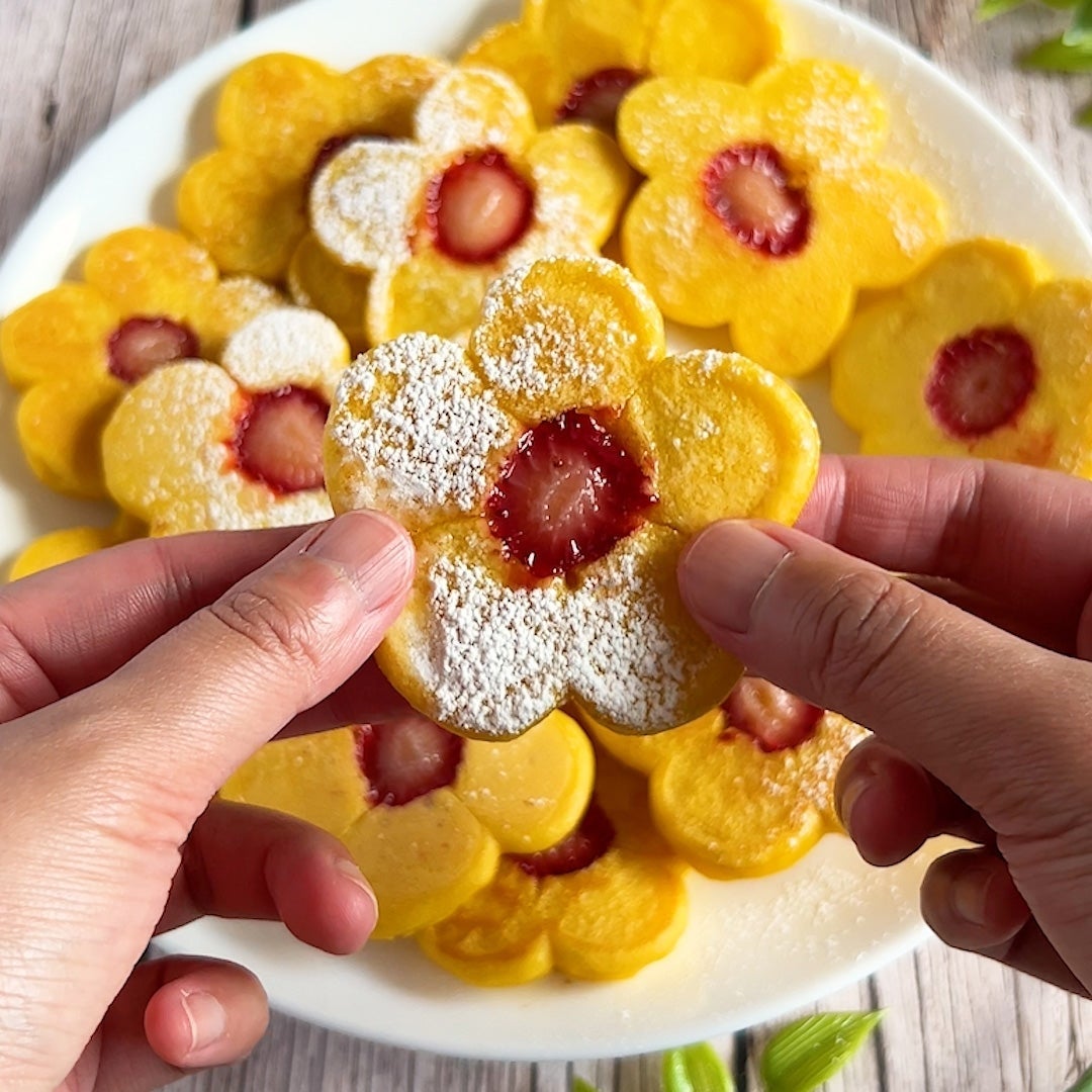 花形のパンケーキを手に持つ。中心にイチゴがのっており、粉砂糖が振りかけられている。