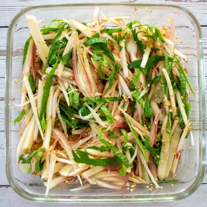細切り野菜とハーブで作られたサラダがガラスのボウルに盛り付けられ、ゴマがトッピングされています。
