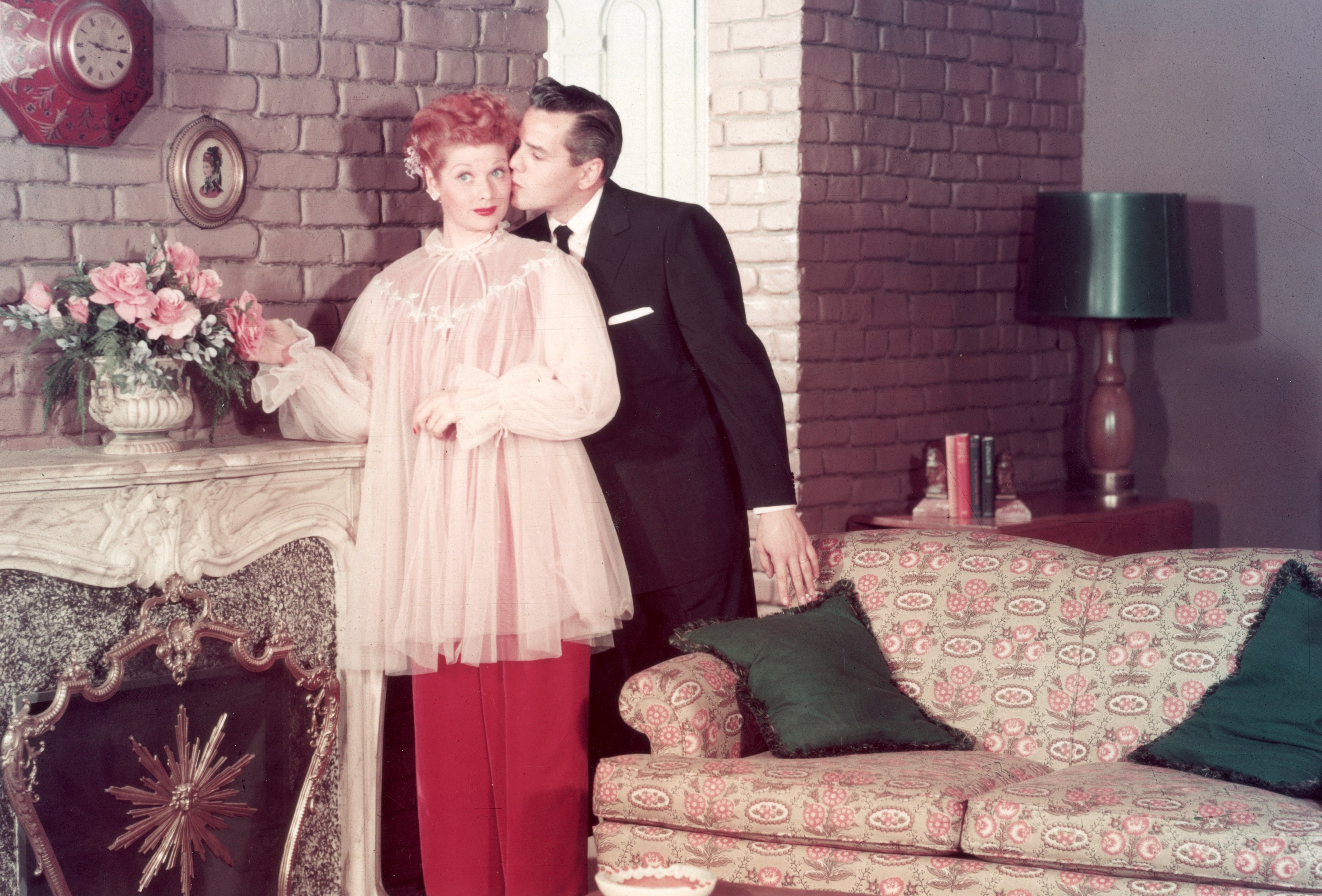 Classic TV scene with a woman in a tulle top and a man in a suit, in a retro living room. Man kisses woman on the temple. 1950s style