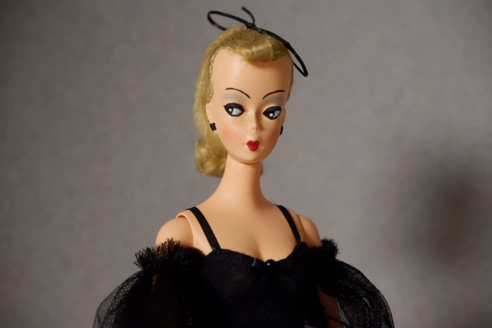 Vintage toy doll with short blonde hair, styled in an elegant black dress with tulle details and a tiny hat