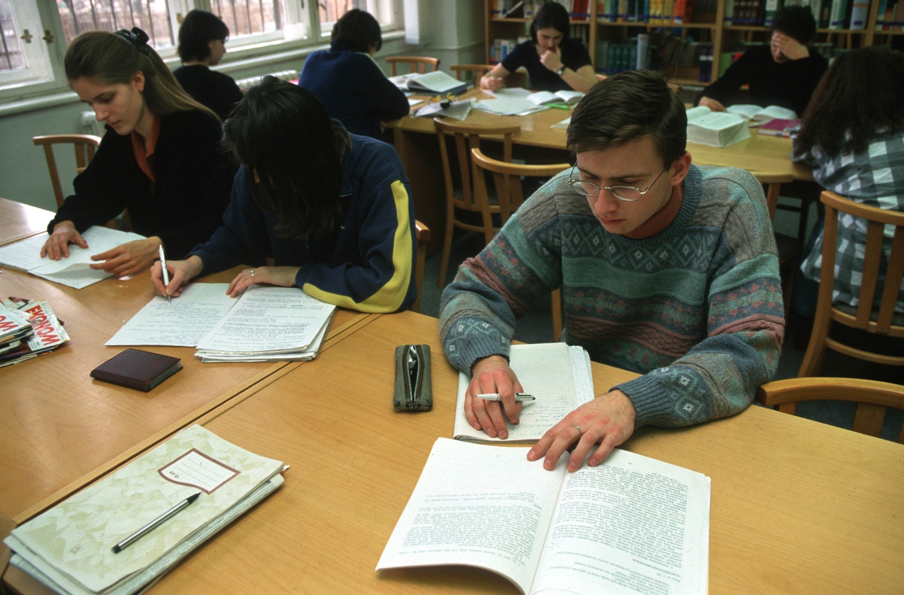 People studying at a library, seated at tables with books and notebooks