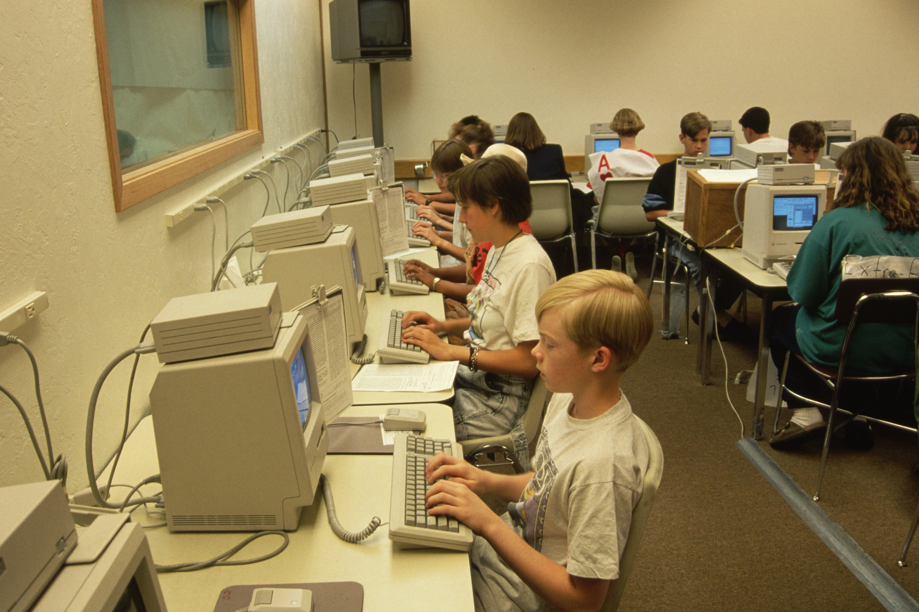 Students in a classroom sit at desks, each working on a computer, focused on their screens