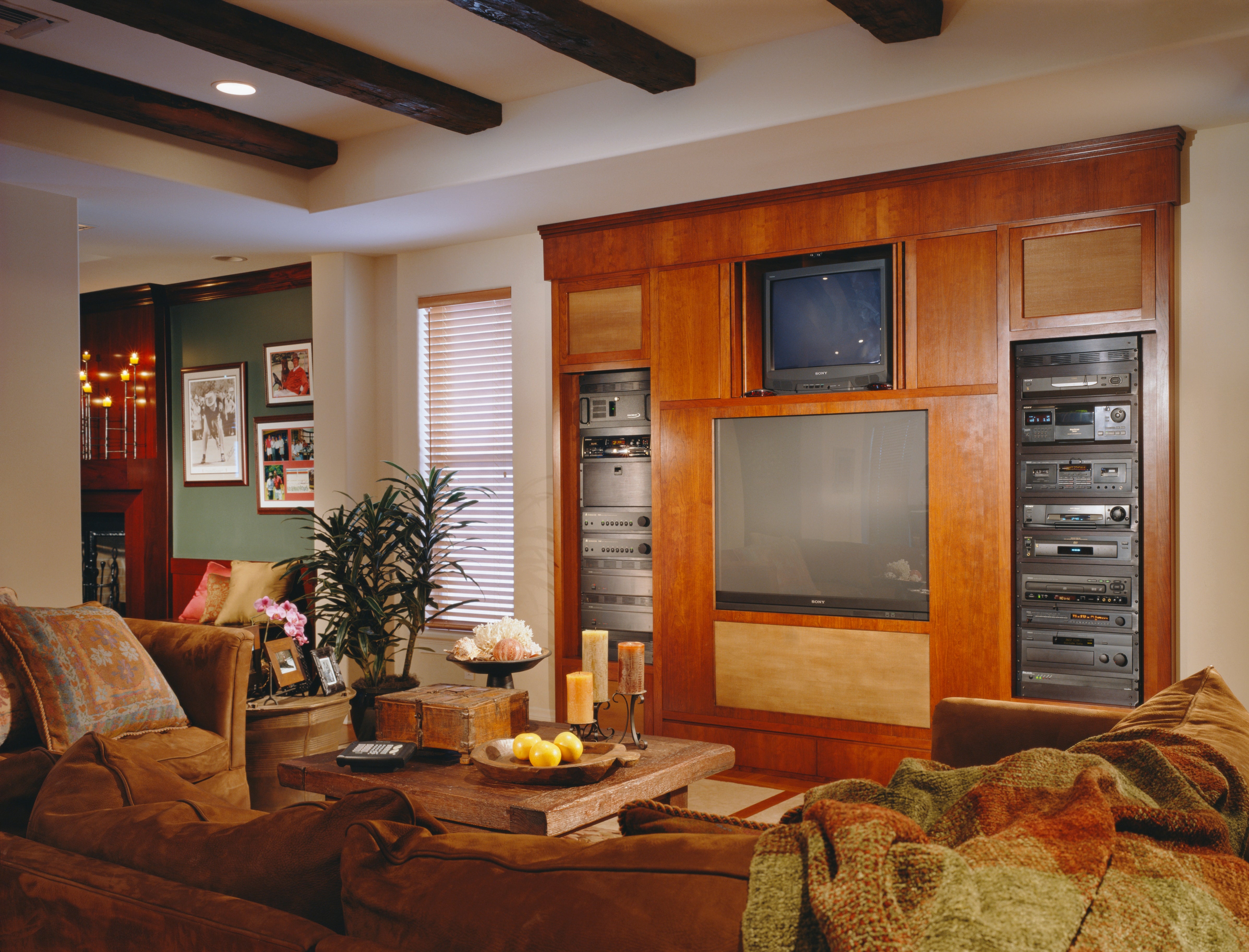 Living room with large wooden entertainment center housing a TV and audio equipment. Cozy seating area with a coffee table and decorative plants