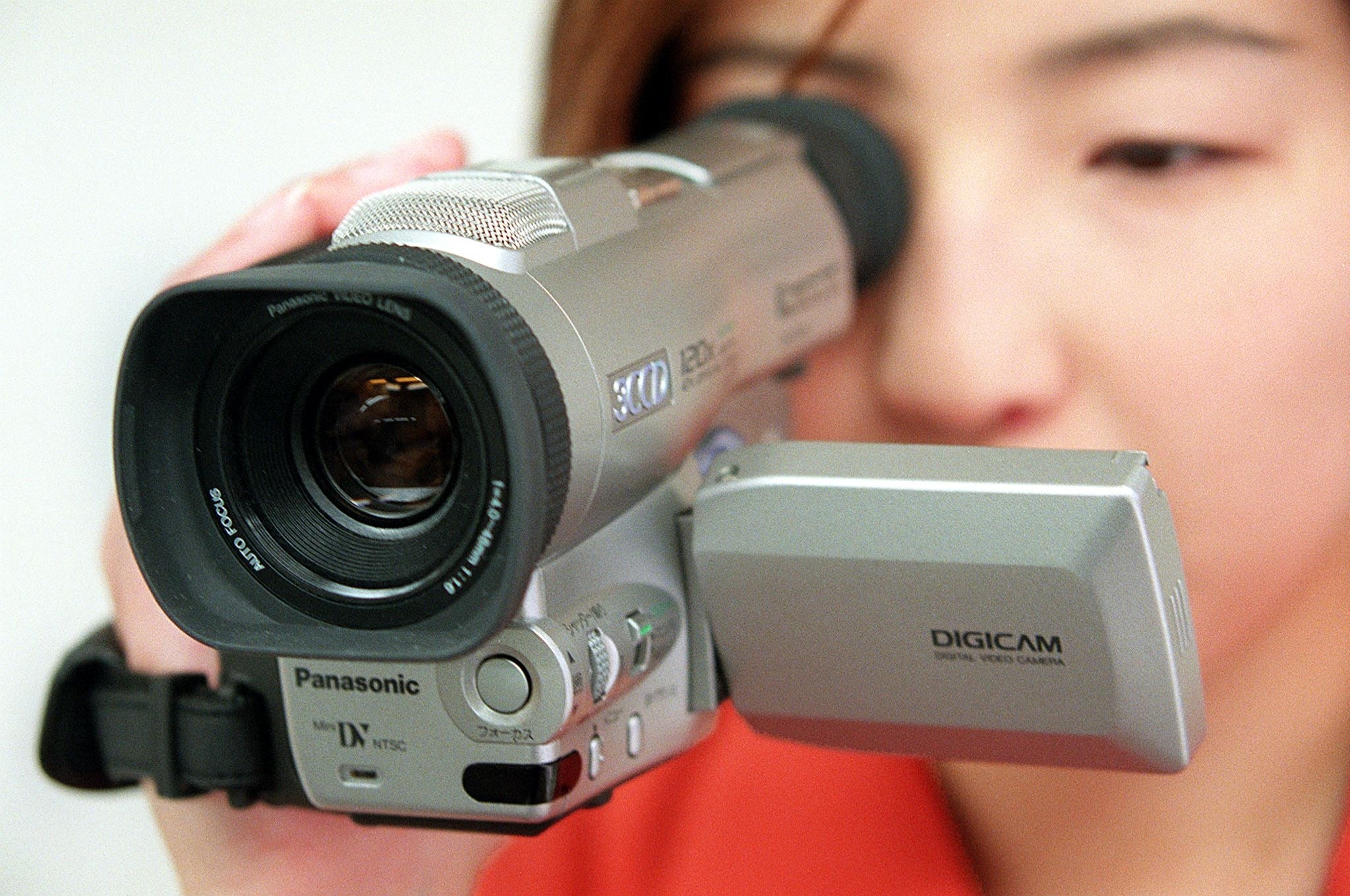 Person using a Panasonic camcorder, focusing on the lens, face partially visible