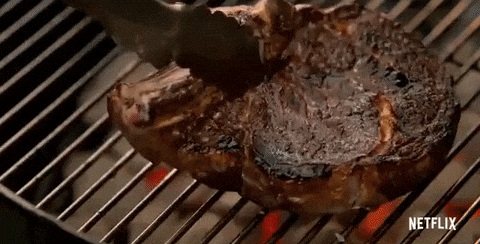 A juicy steak sizzles on a grill with flames beneath, being flipped with tongs