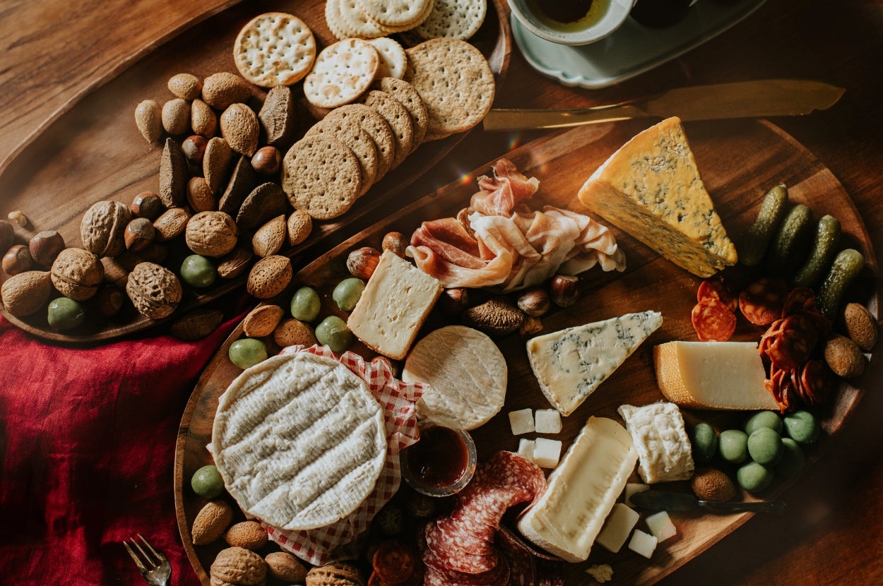 Assorted cheese and charcuterie board with crackers, nuts, meats, olives, and grapes, arranged on a wooden platter