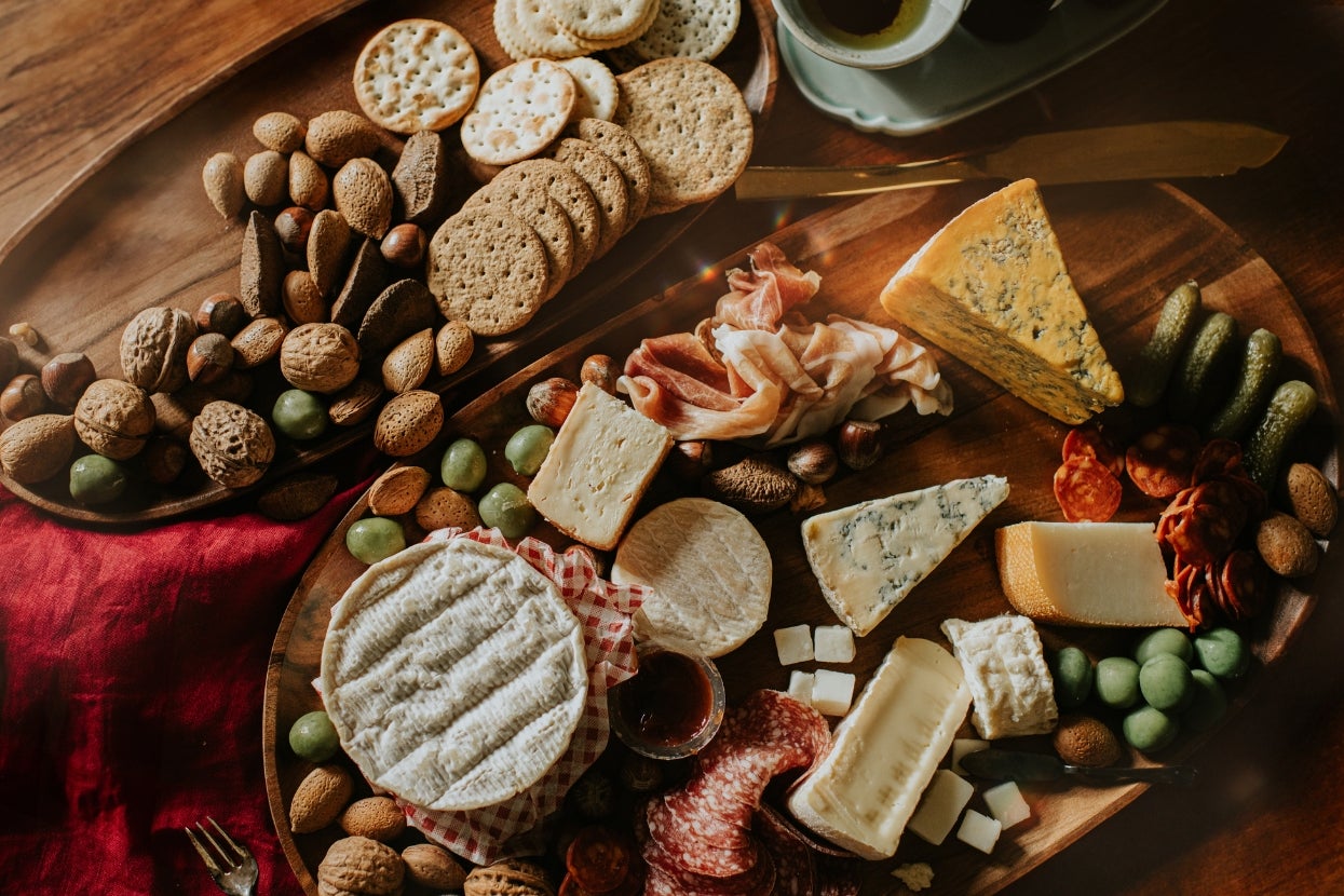 Assorted cheese and charcuterie board with crackers, nuts, meats, olives, and grapes, arranged on a wooden platter