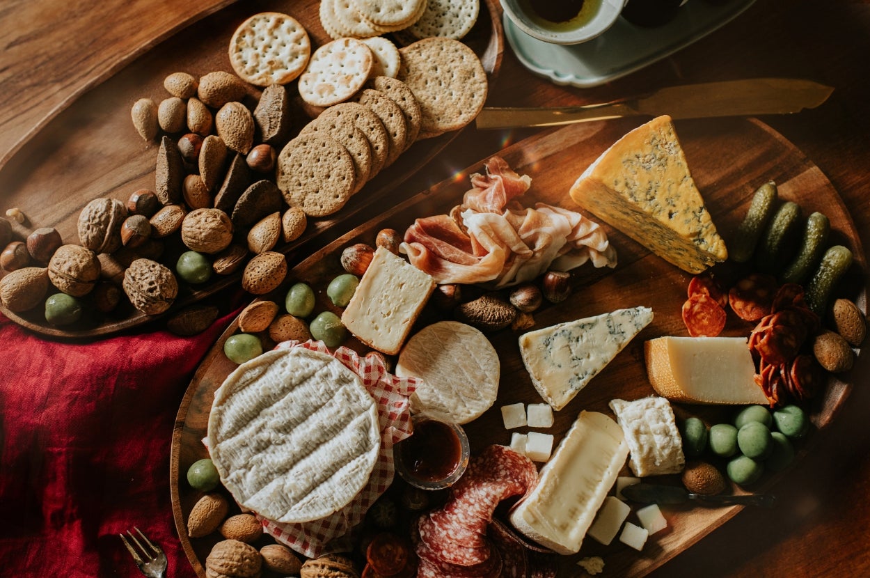 Assorted cheese and charcuterie board with crackers, nuts, meats, olives, and grapes, arranged on a wooden platter