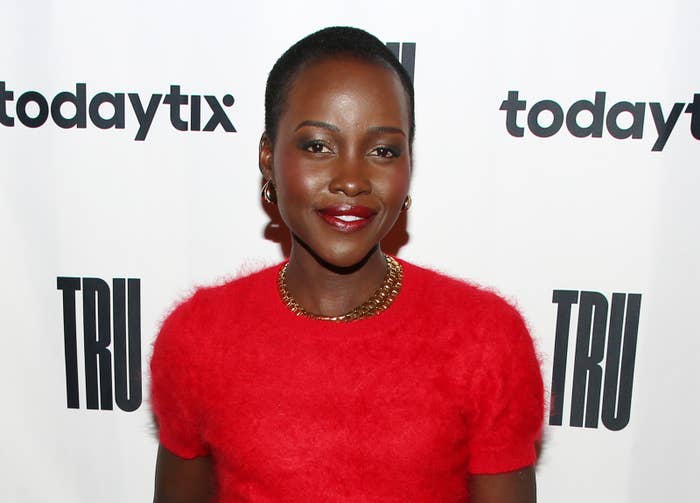 Person in fuzzy, red top on event red carpet, smiling, against a backdrop with "todaytix" and "TRU" logos