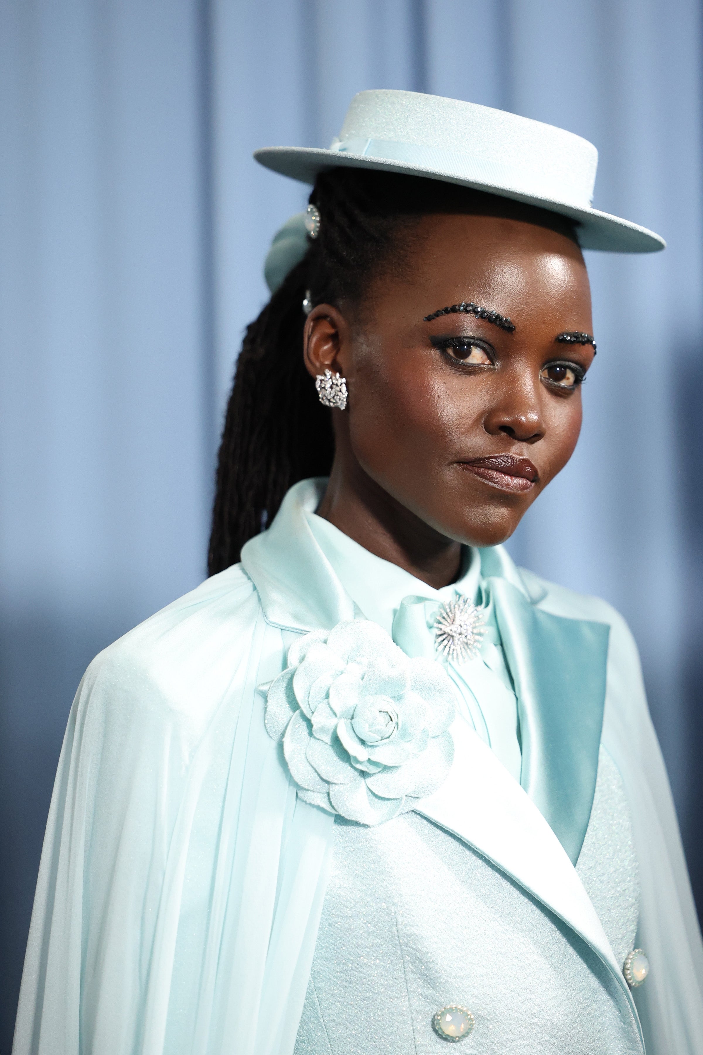 Person in elegant suit with floral detail and a brimmed hat at an event
