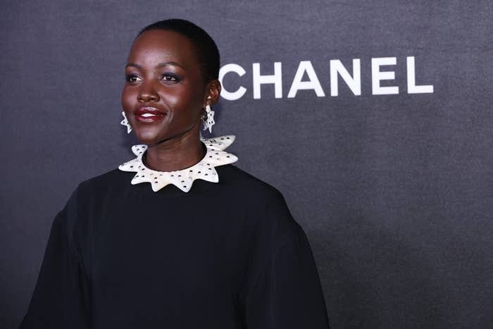 Celebrity at an event wearing a stylish dress with a ruffled collar and statement earrings, standing against a Chanel-branded backdrop