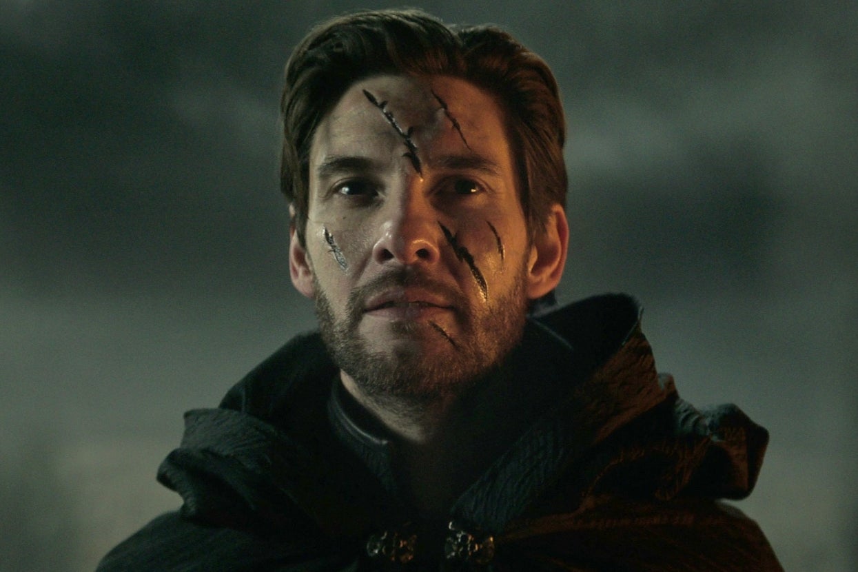 Benjamin Barnes as the Darkling in "Shadow and Bone" with a cloak and facial scars stares ahead in a dramatic, moody setting