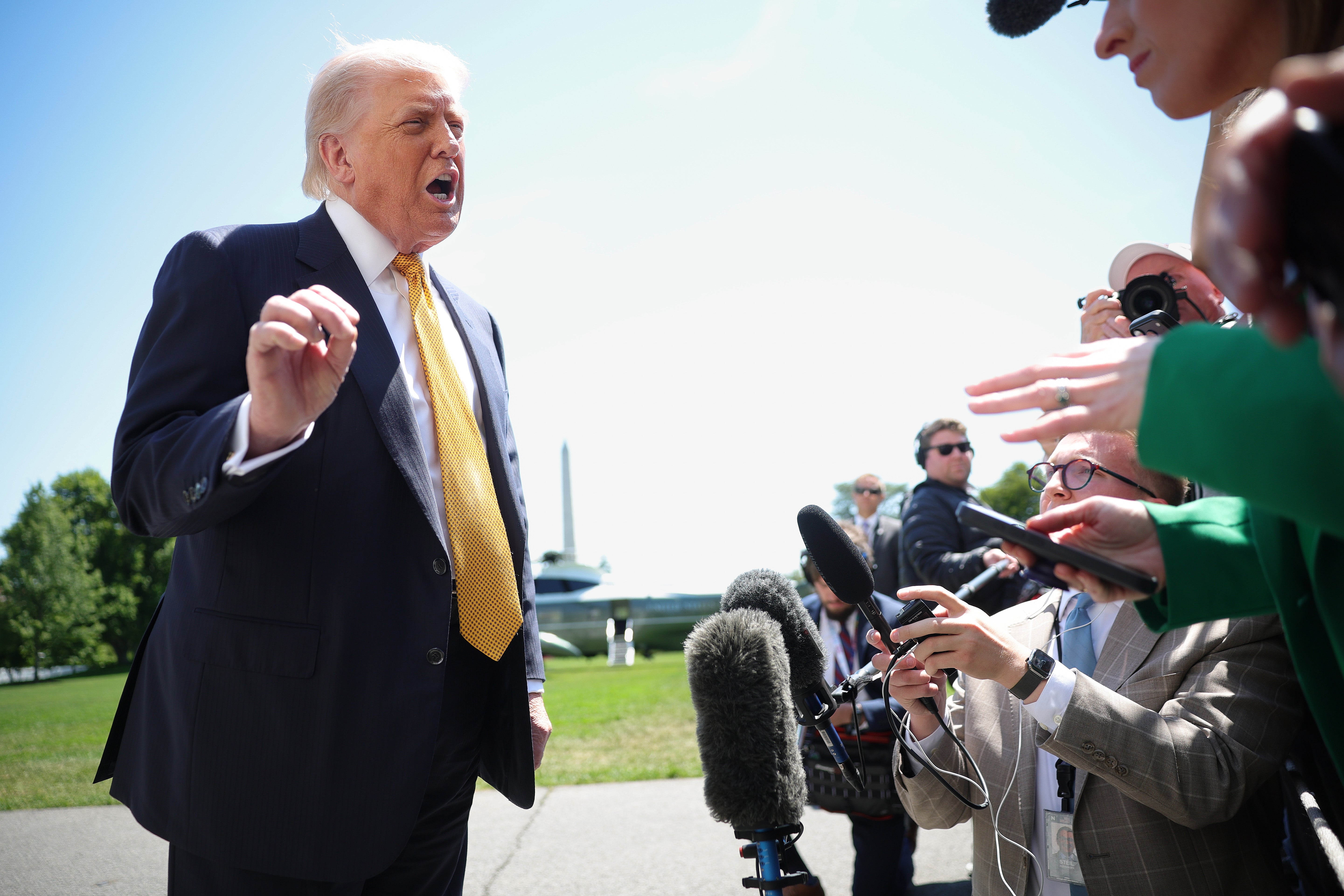 A person speaking to reporters outdoors with microphones and cameras pointed toward them