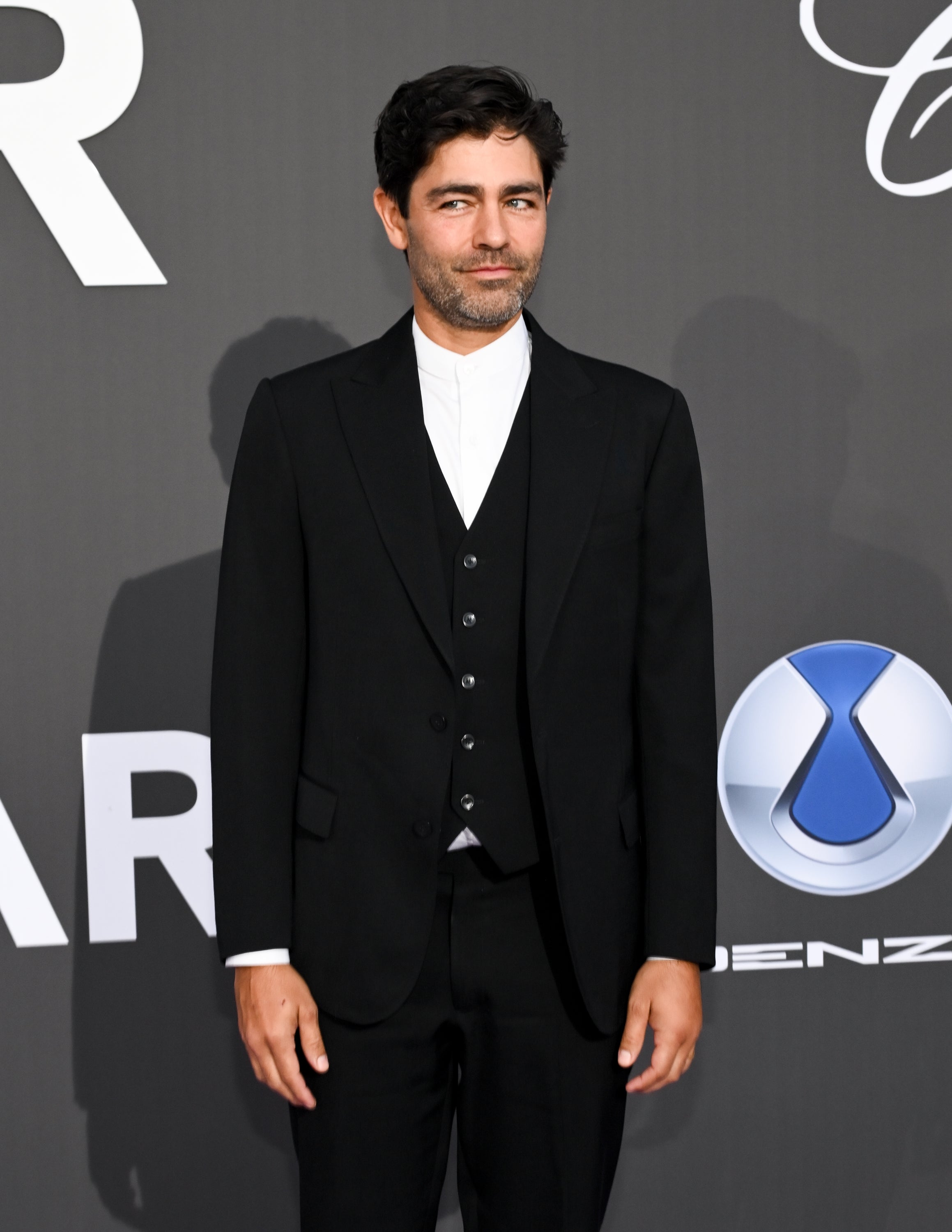 Man in a formal black suit with a three-piece style, standing on a red carpet