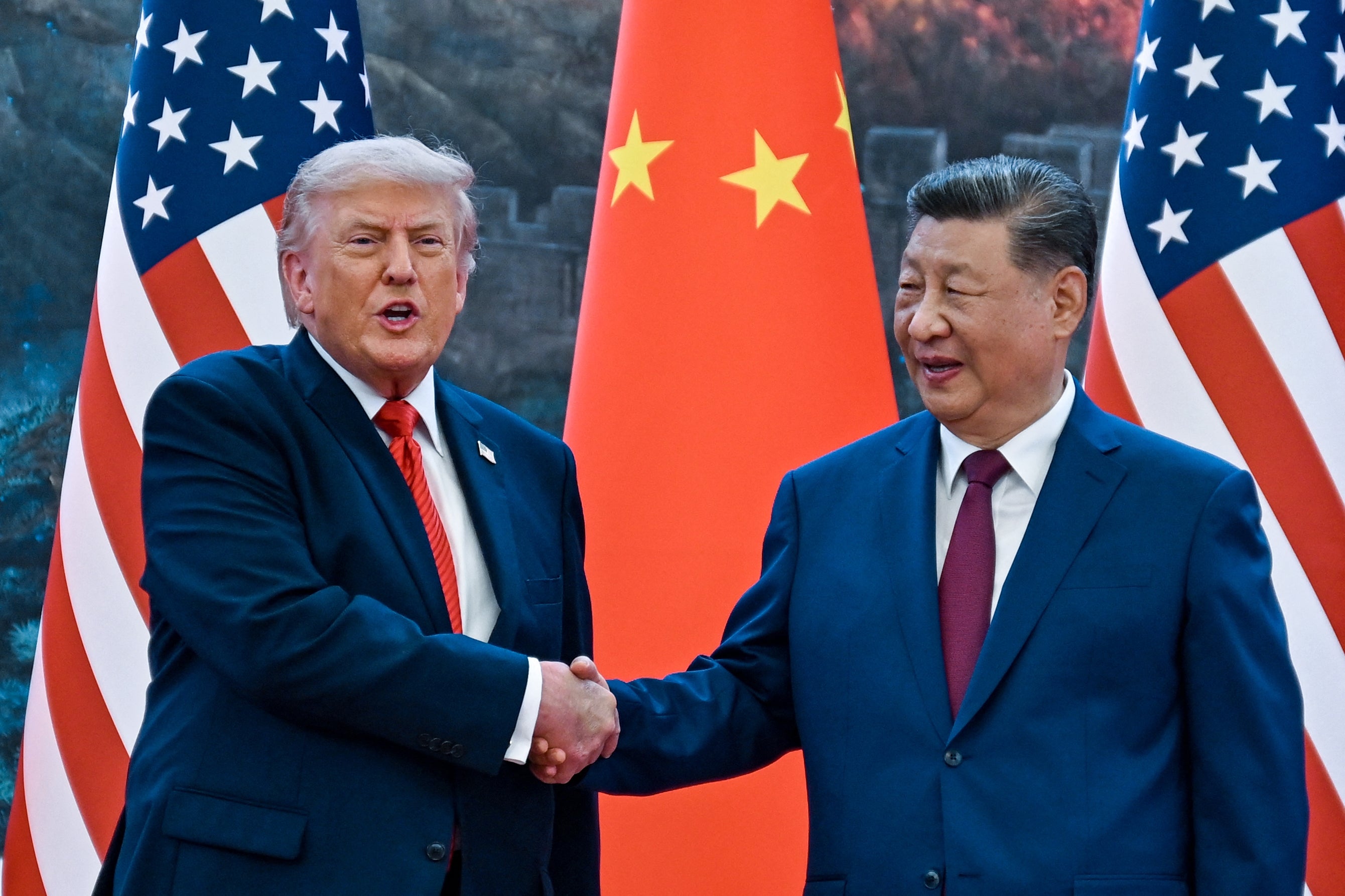 Two men in formal suits shake hands in front of U.S. and Chinese flags