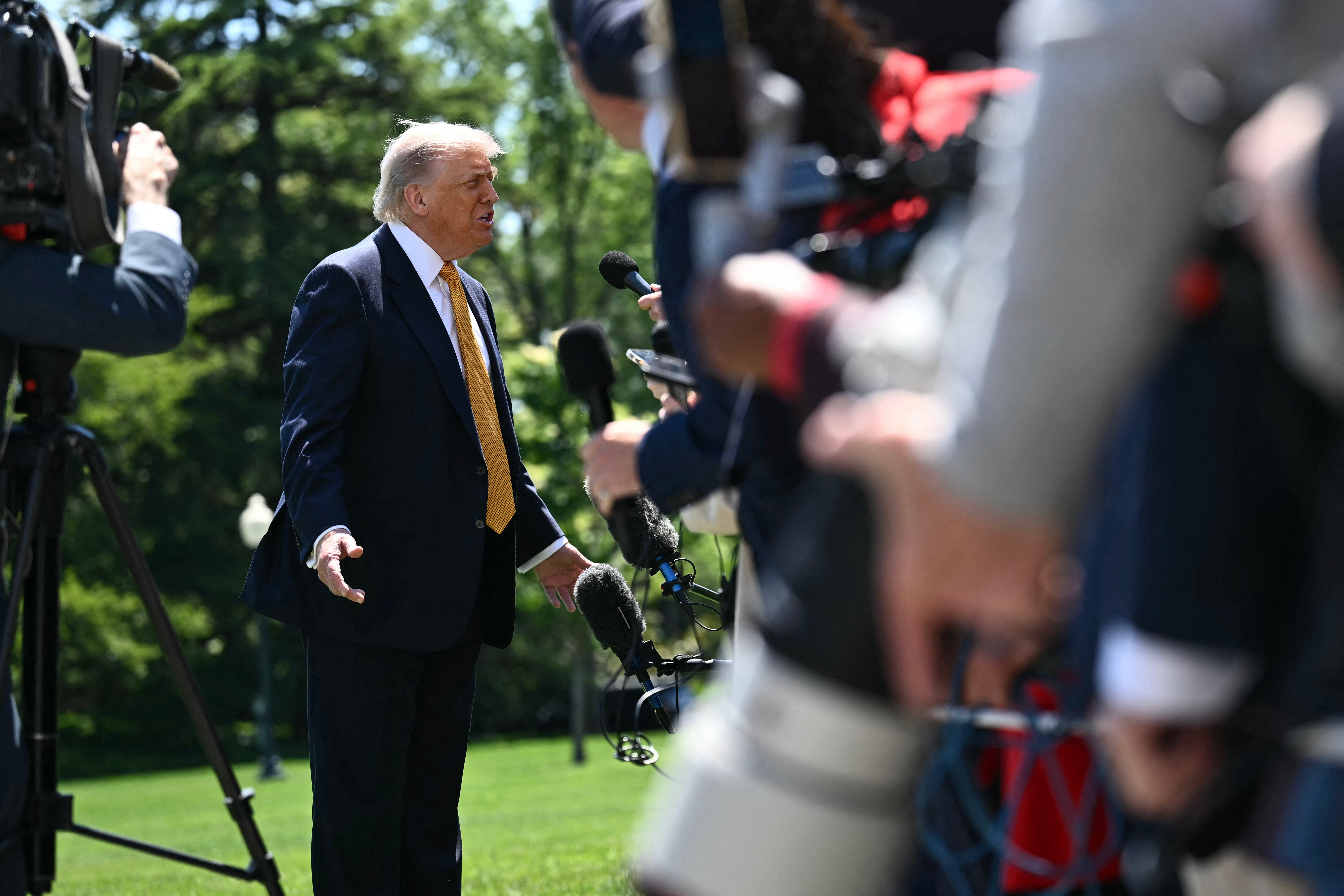 Person in a suit speaks to reporters and microphones outdoors, suggesting a press interaction