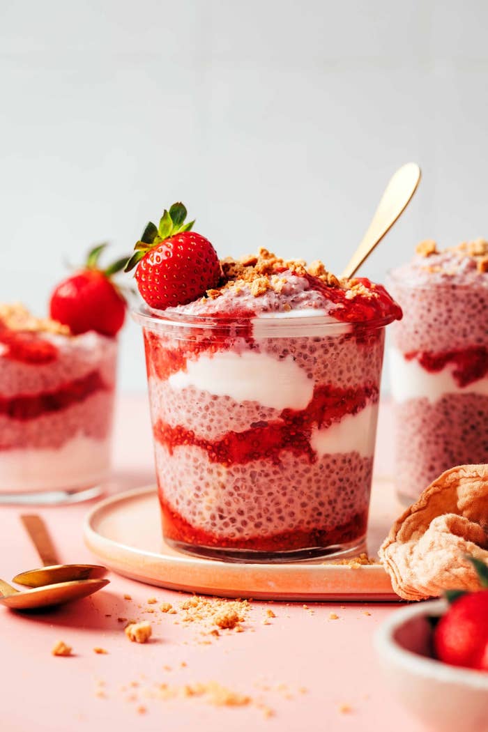 Layered chia pudding with strawberries, cream, and crunchy toppings in a glass, garnished with a whole strawberry on top