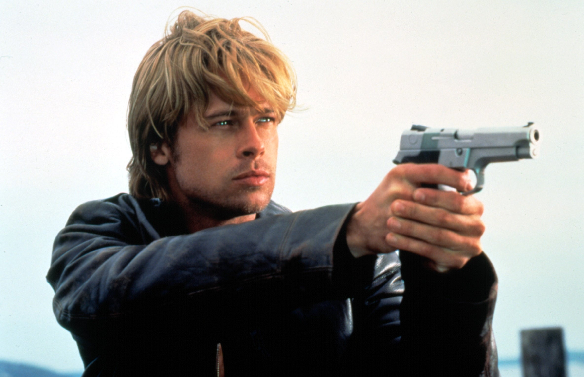 A idiosyncratic   with medium-length hair, wearing a leather jacket, holds a handgun portion    looking intently into the distance