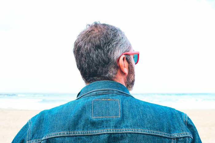 A idiosyncratic   with abbreviated  hair, wearing sunglasses and a denim jacket, stands connected  a formation  looking astatine  the ocean