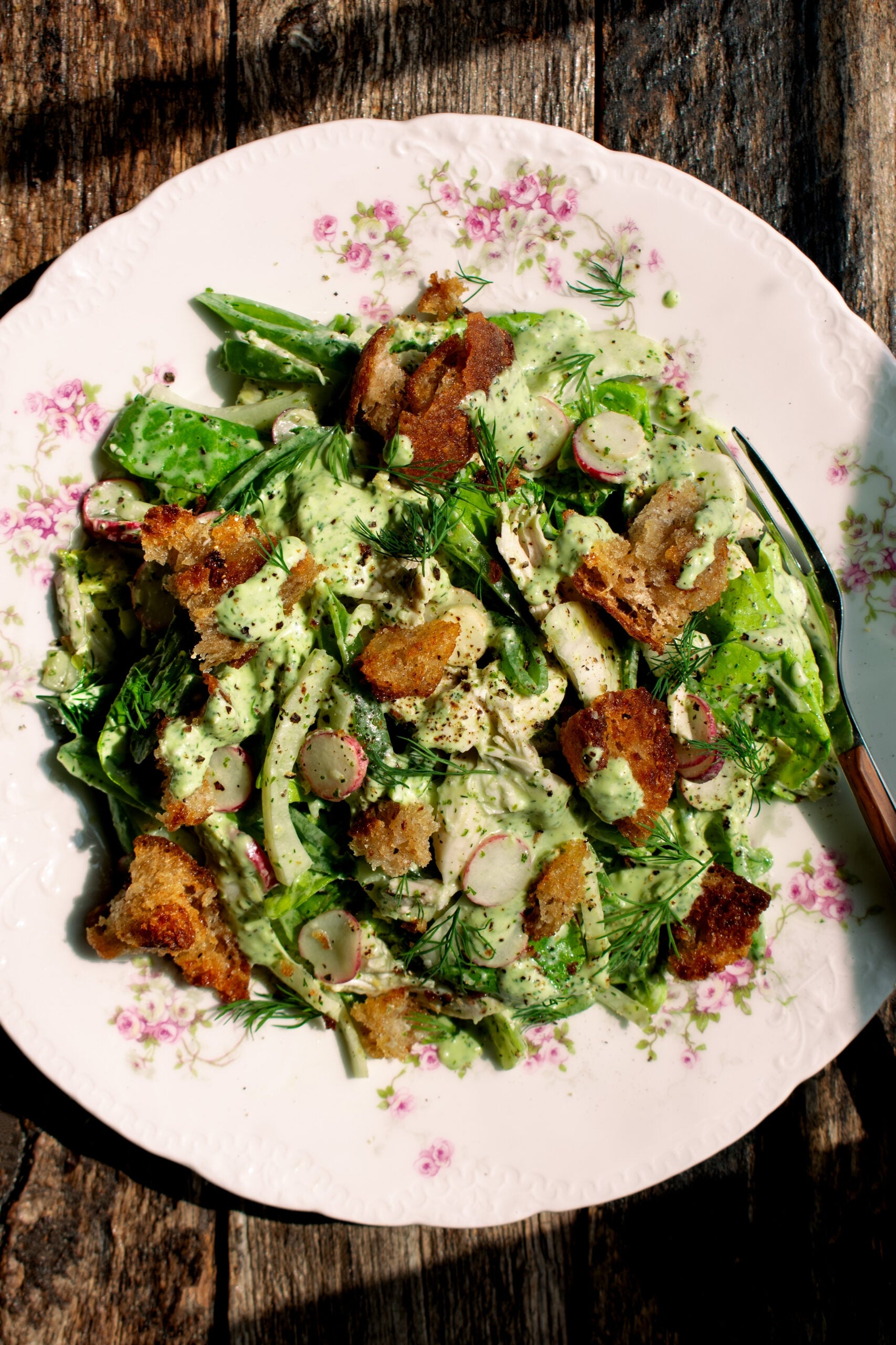 Fresh salad on a floral plate with radishes, leafy greens, dill, croutons, and creamy dressing