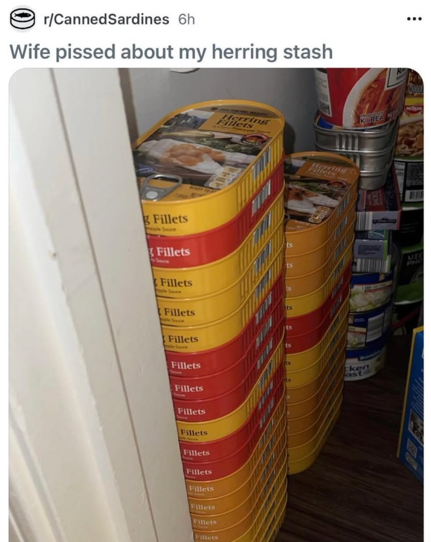 Stacked tins of herring fillets fill a pantry closet, posted with a humorous caption about a spouse's reaction