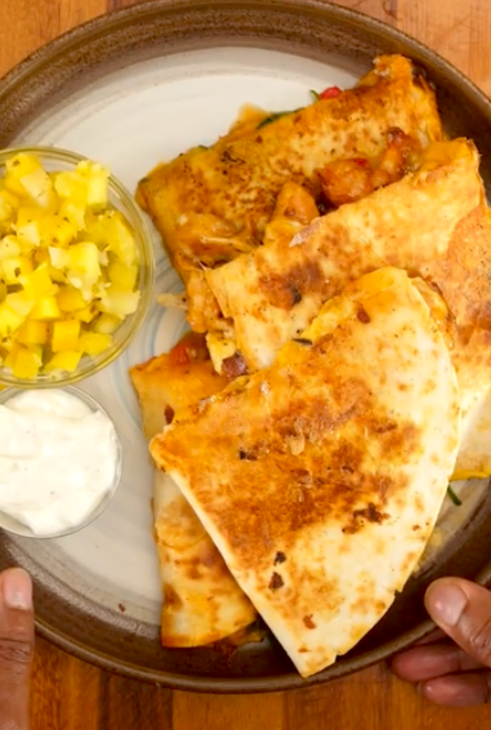 Quesadillas filled with grilled vegetables and cheese on a plate, served with mango salsa and sour cream