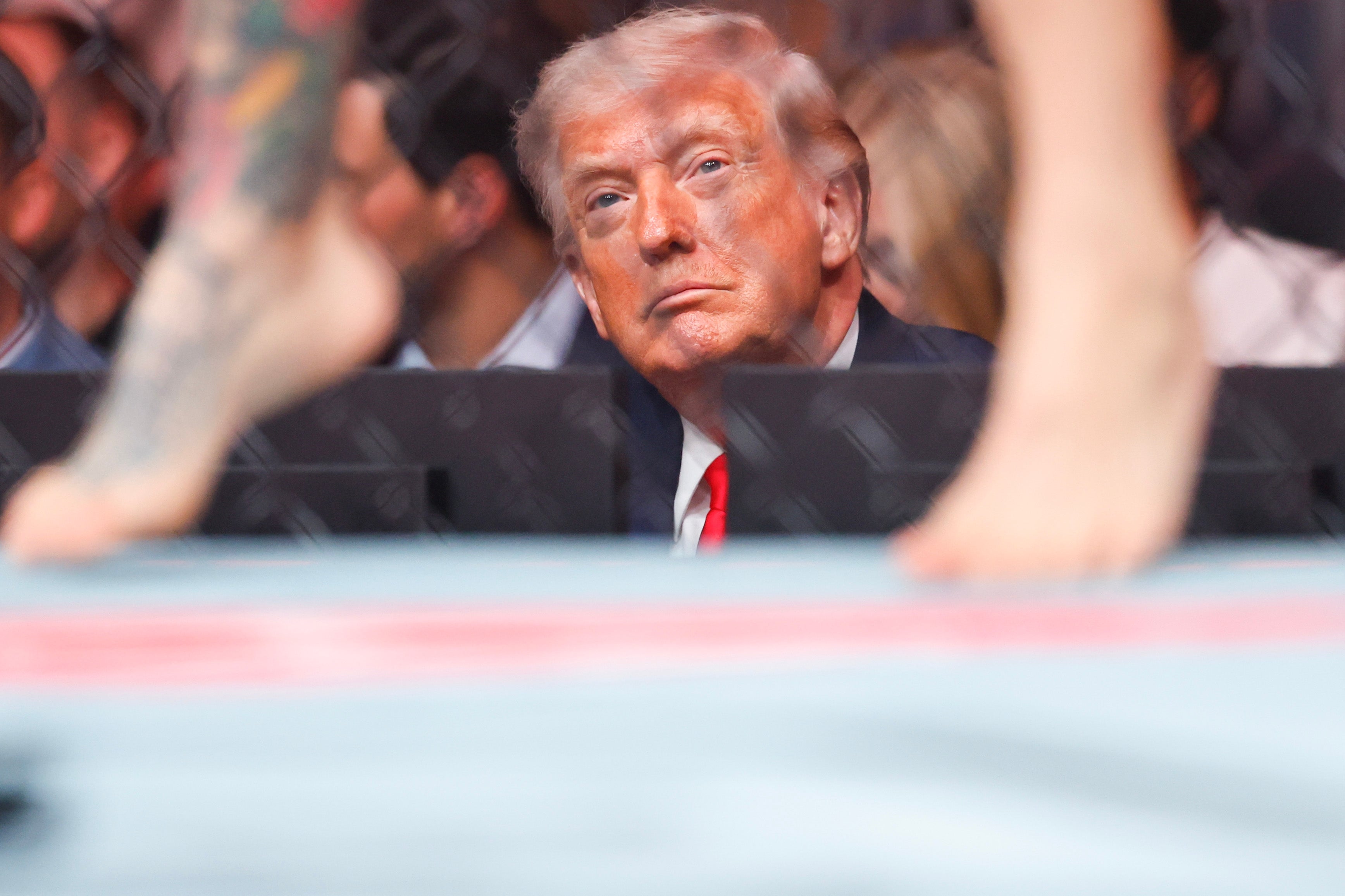 Person sitting behind a combat sports ring, observing a match, with fighters in the foreground