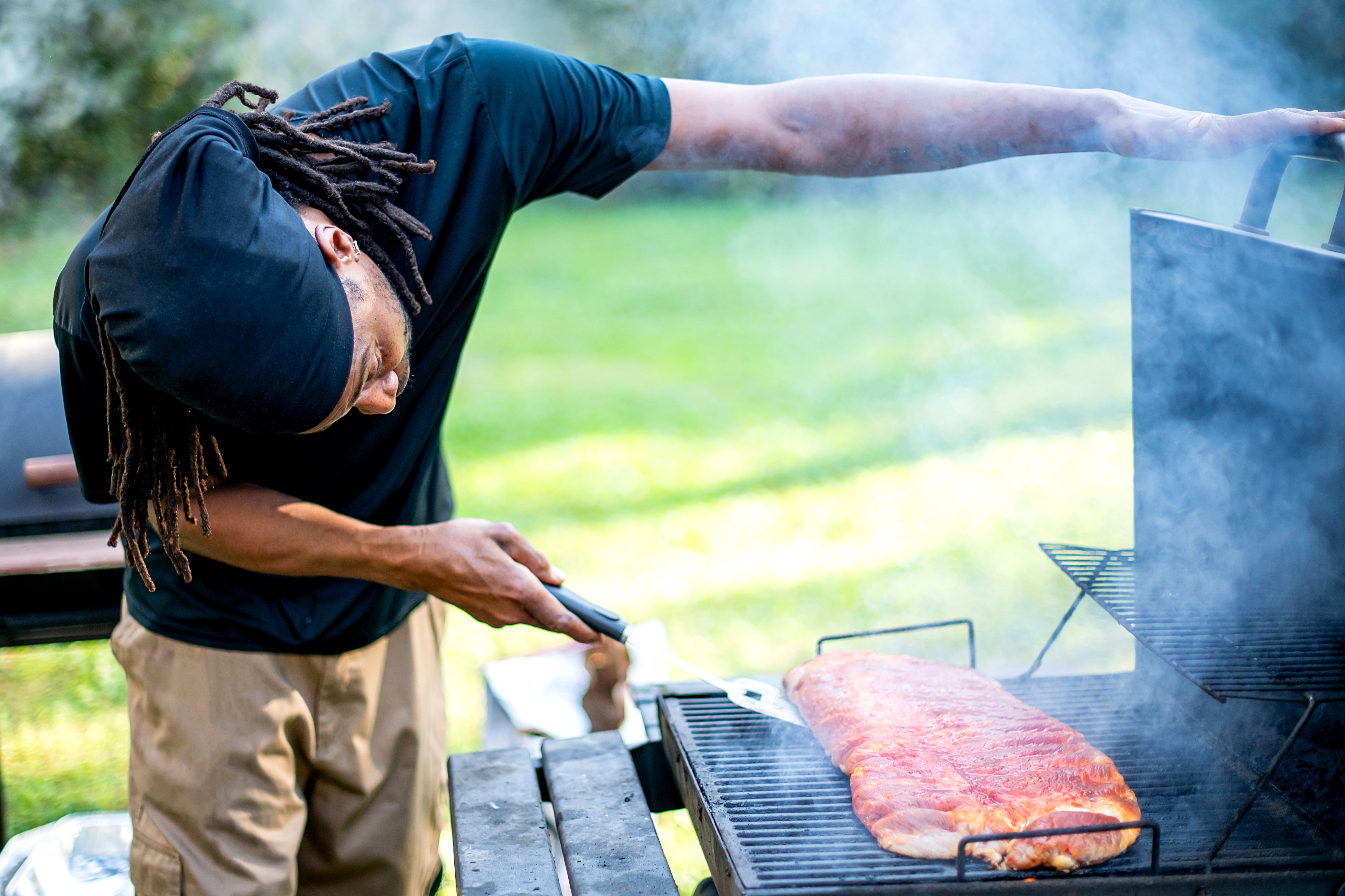 Person grilling ribs outdoors, focusing connected cooking process, with fume rising from the grill