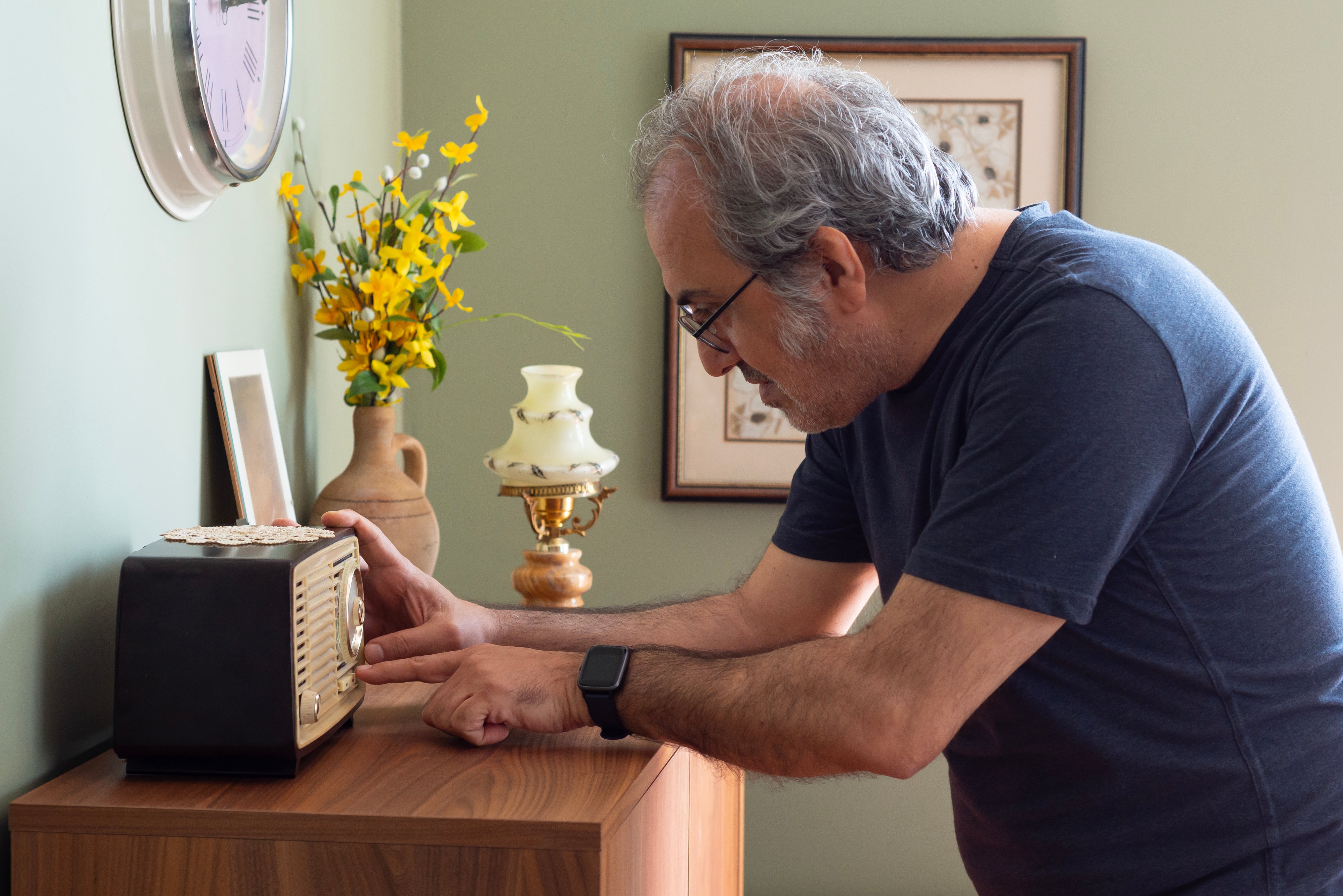 An older big adjusts a vintage vigor connected a woody table, with a vase and lamp successful the background, illustrating attraction to nostalgic technology