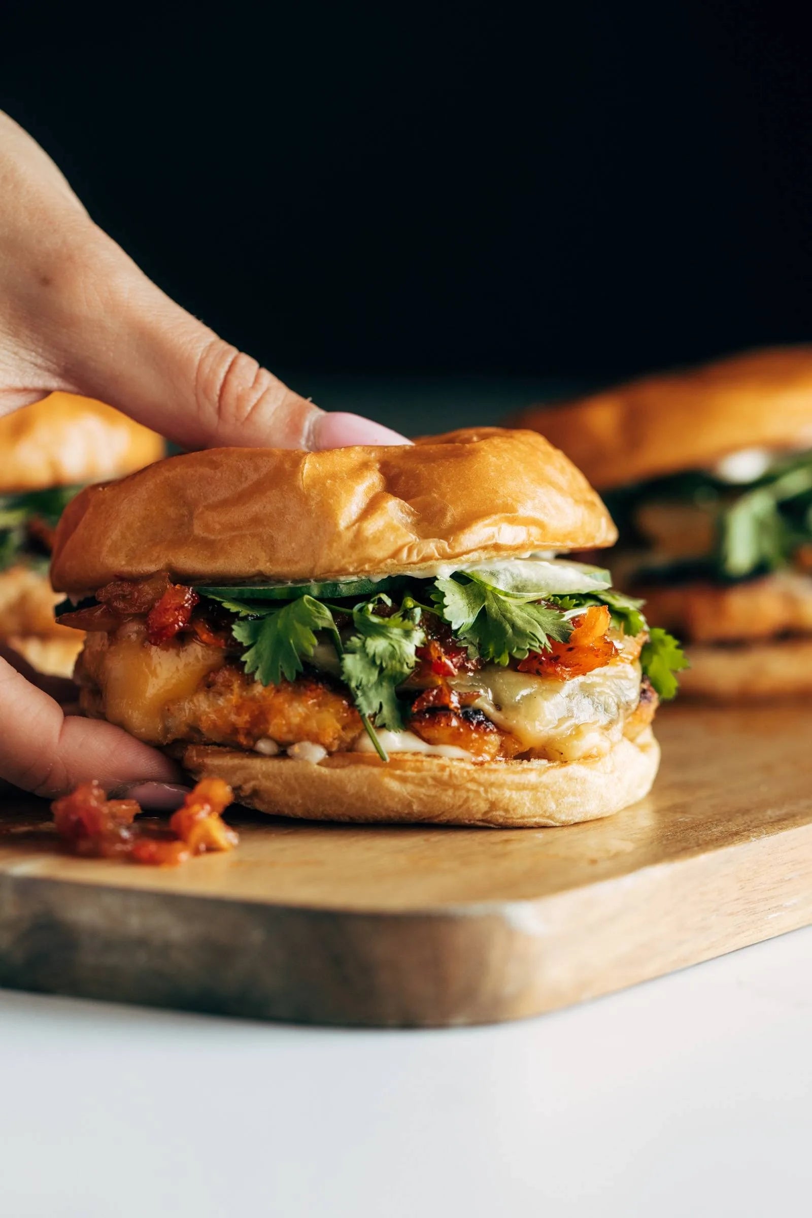 Hand holding a gourmet burger with lettuce, cheese, and salsa on a wooden board