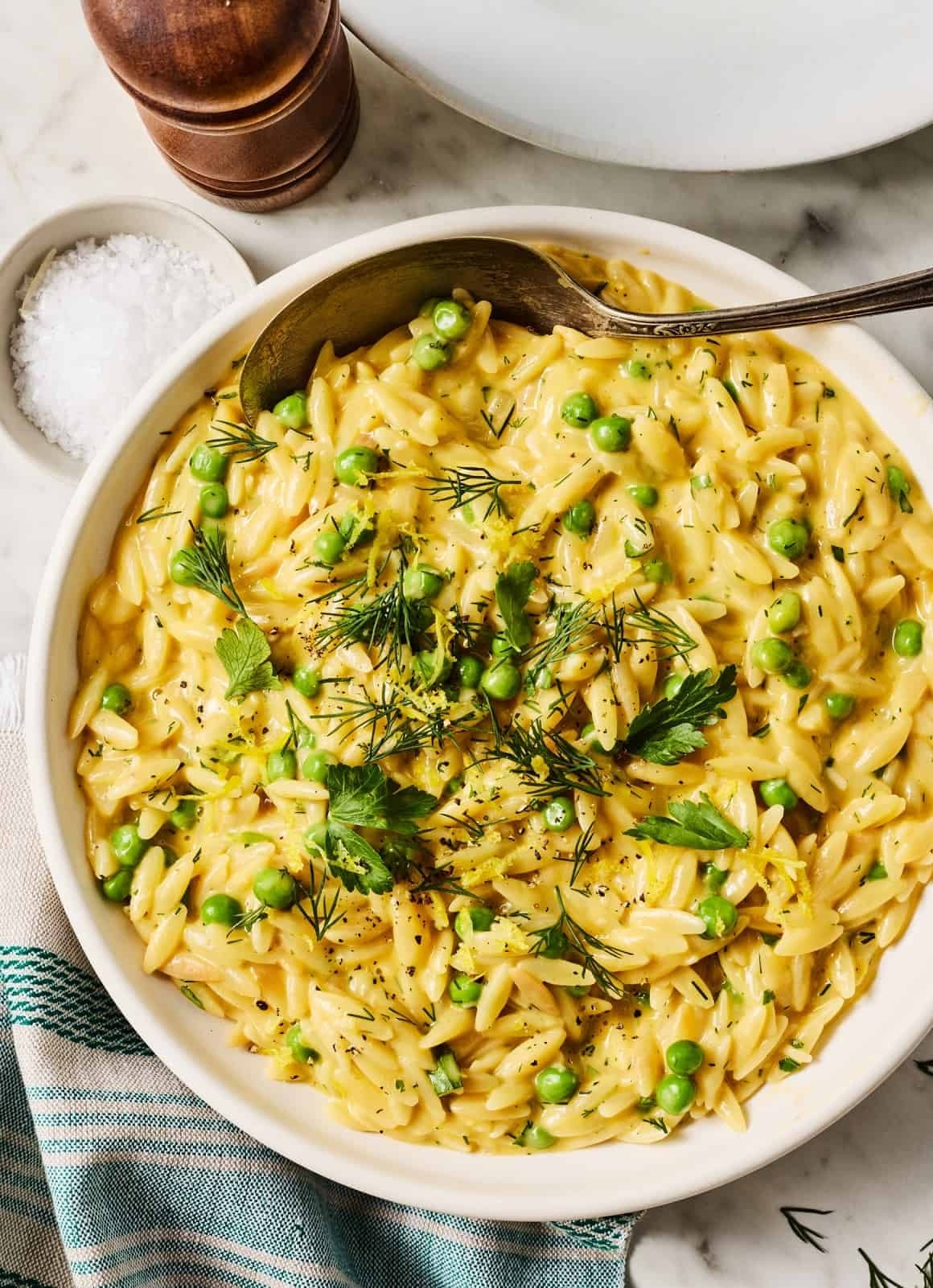 A bowl of creamy orzo pasta with green peas and garnished with fresh herbs