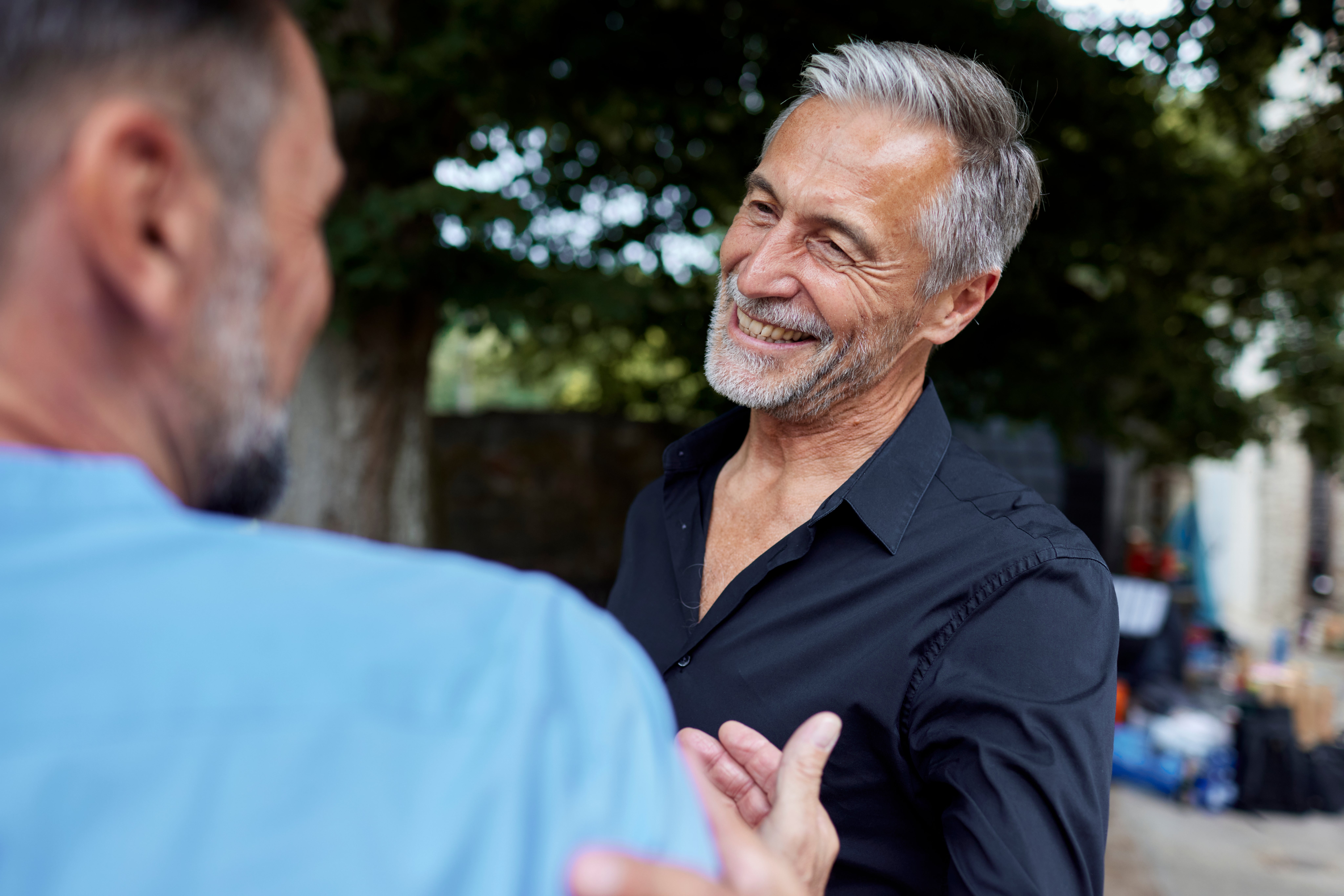 Two men smiling and chatting outdoors; 1 is wearing a achromatic shirt, appearing steadfast and engaged successful a affirmative conversation