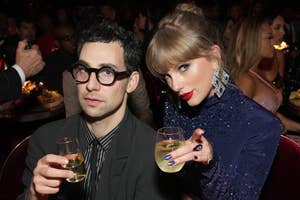 Jack Antonoff in a suit with glasses and Taylor Swift in a sequined outfit hold drinks during an event