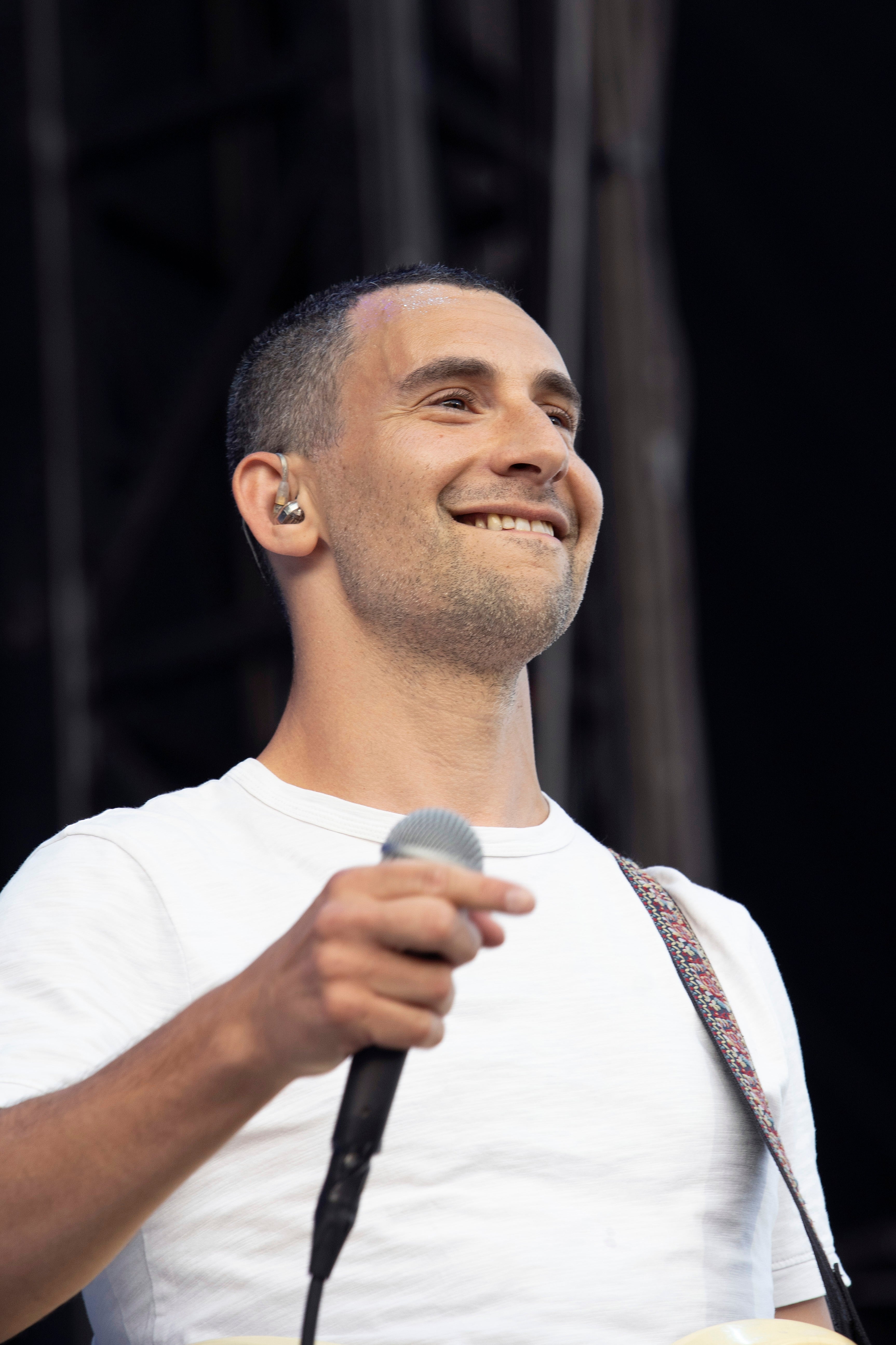 Jack Antonoff connected signifier holding a microphone and smiling, wearing a plain t-shirt and an earpiece