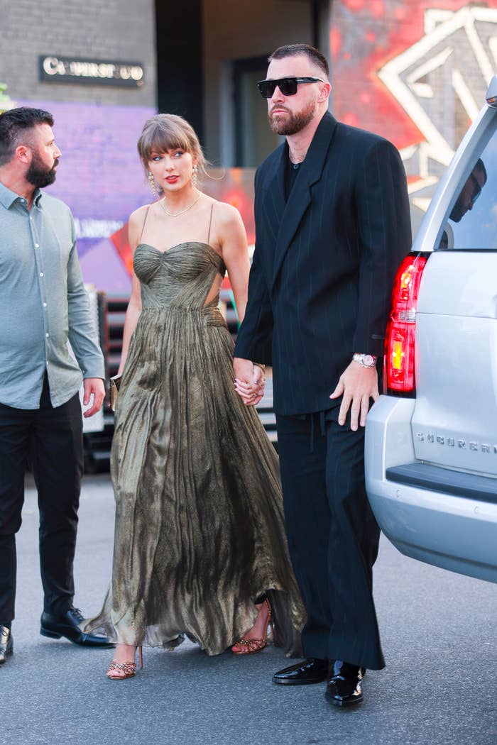 Taylor Swift in a dress and Travis Kelce in a suit walking hand in hand