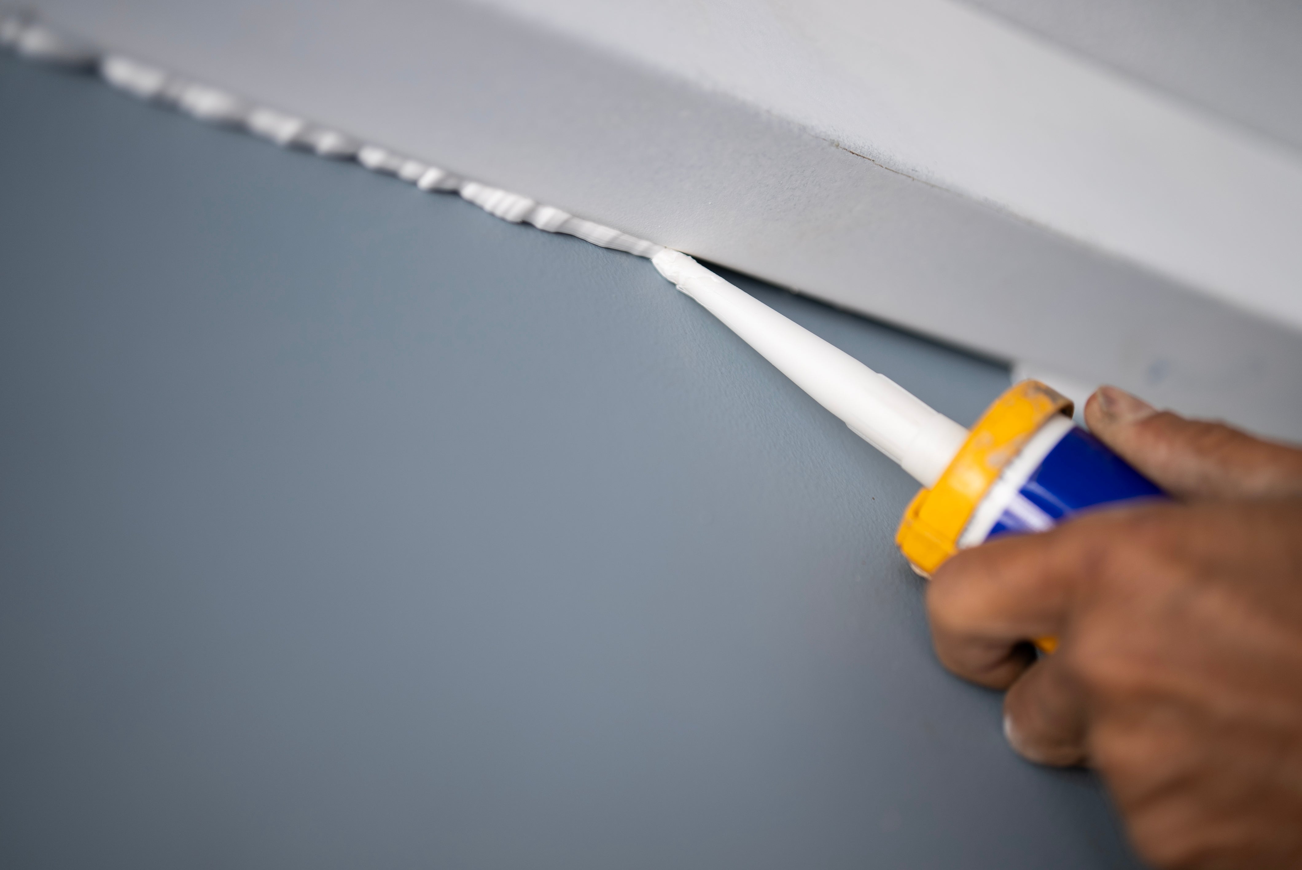 Person applying sealant to a seam with a caulking gun