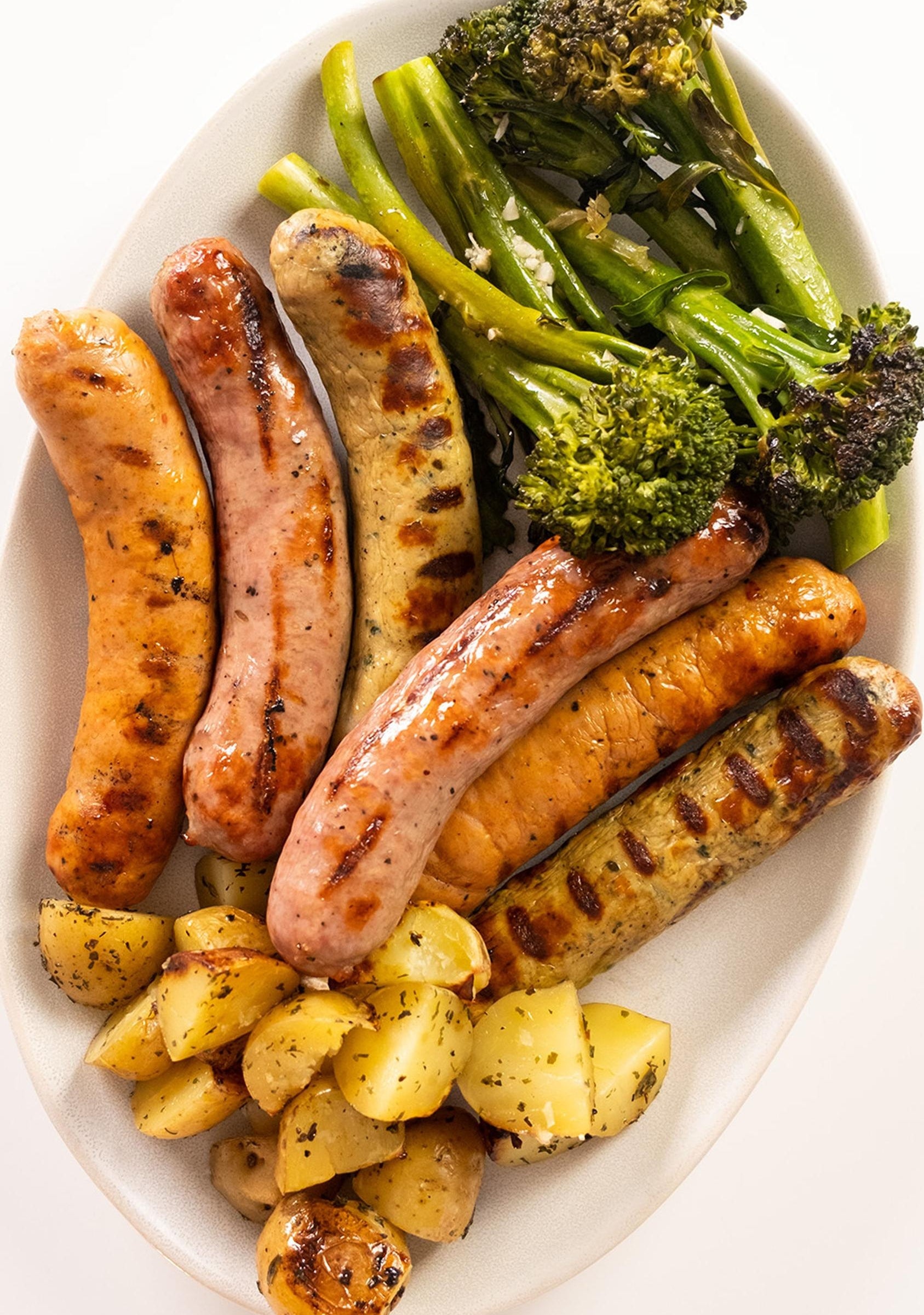 Plate of grilled sausages, roasted potatoes, and broccoli, arranged neatly for a delicious meal presentation