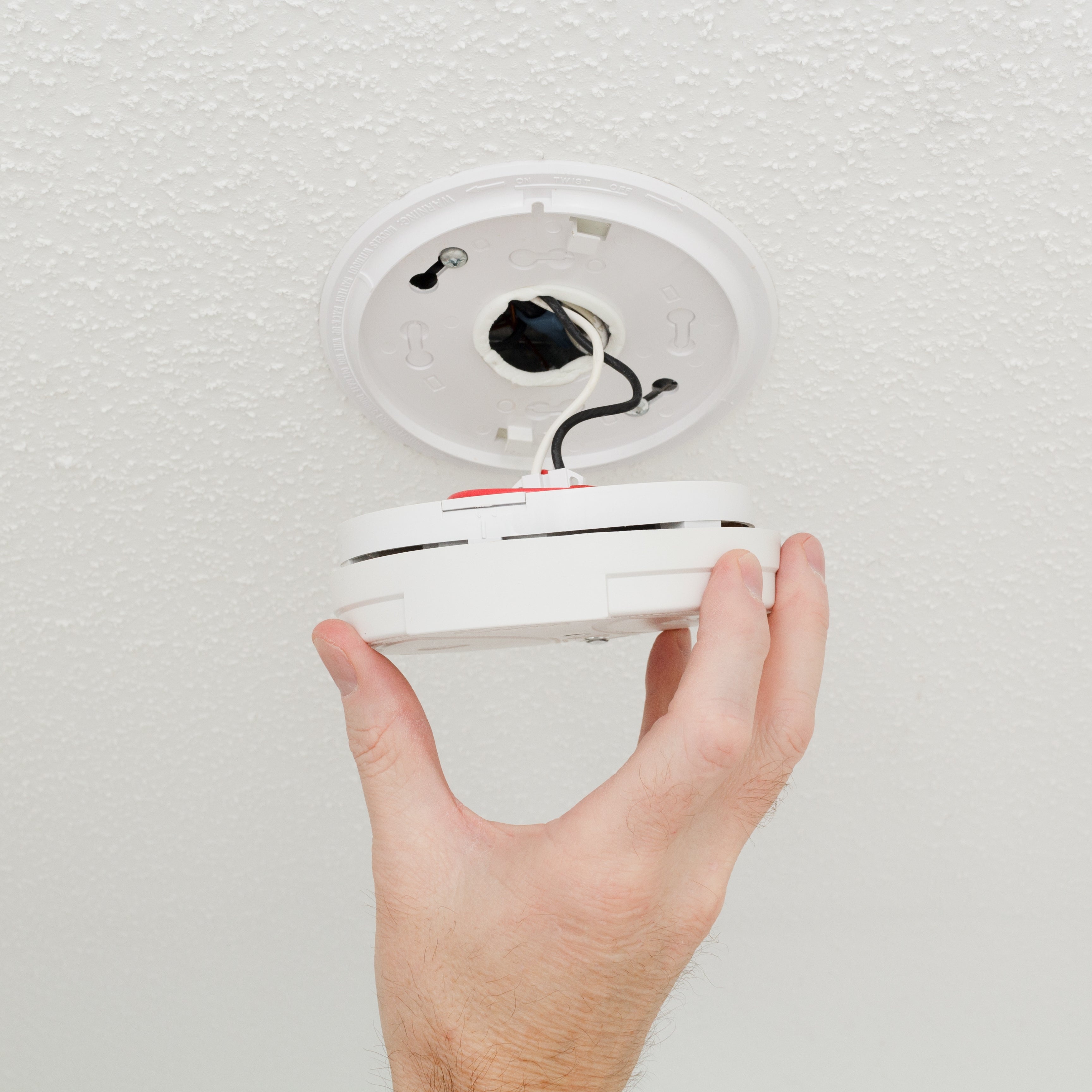 Hand installing or removing a smoke detector from a ceiling