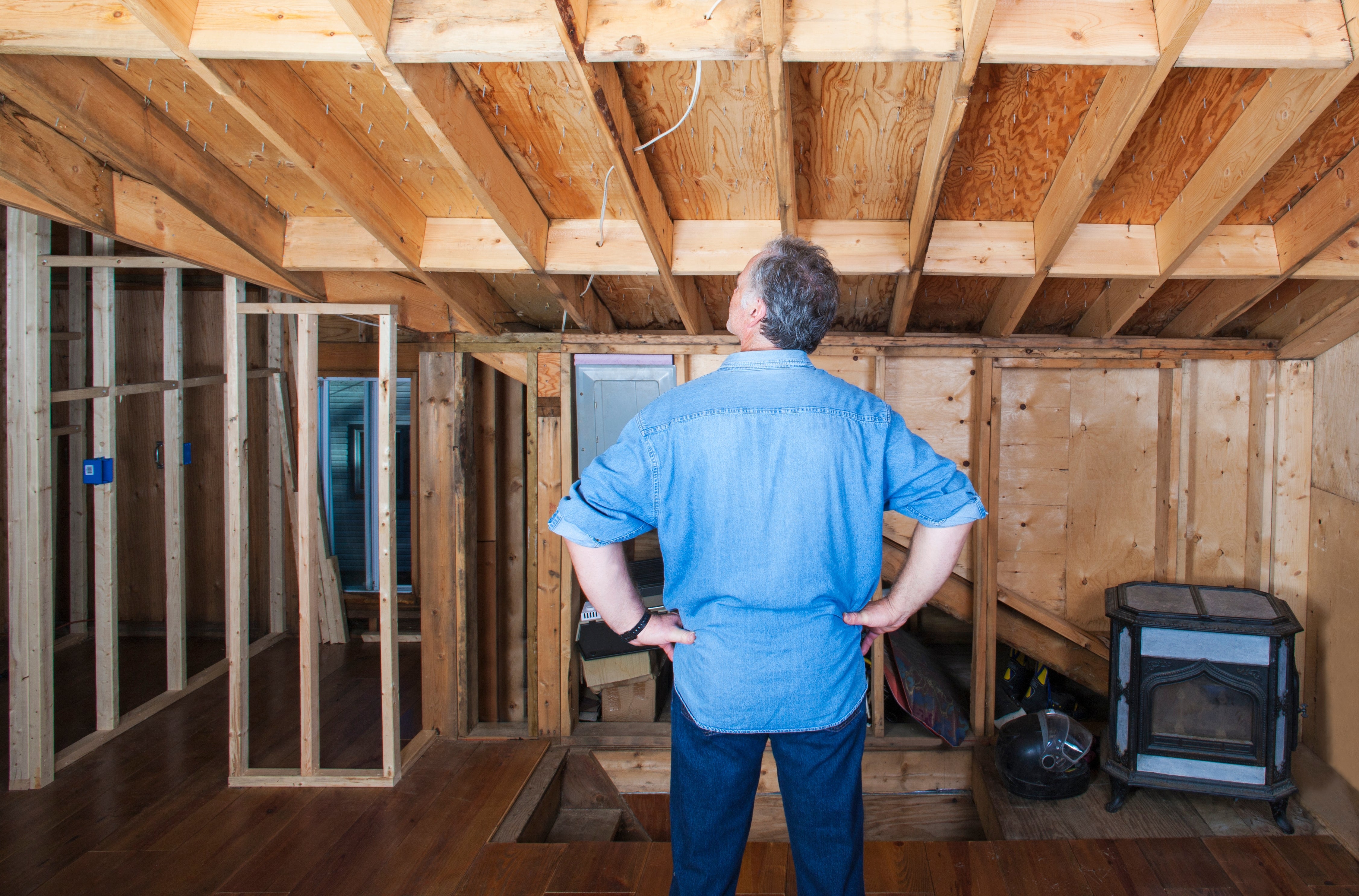 A person in a denim shirt observes the exposed wooden beams and unfinished structure of a room under construction or renovation