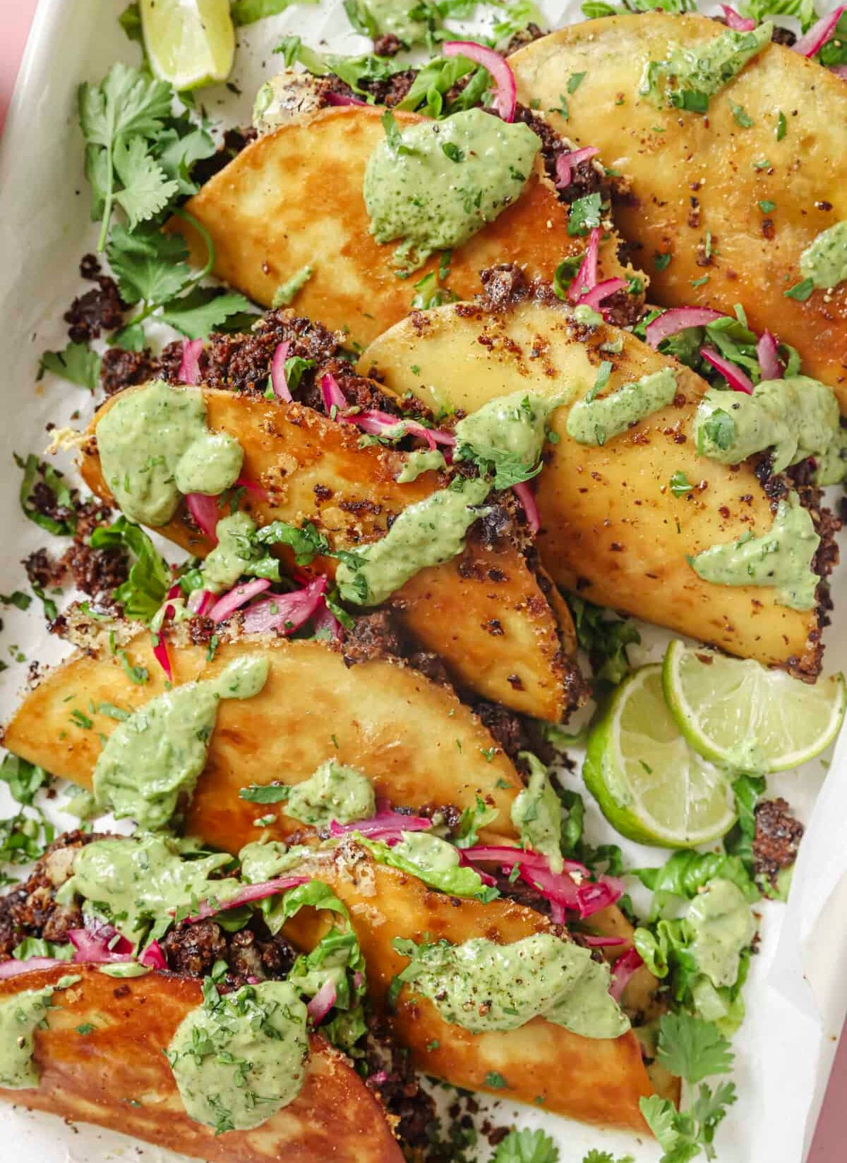 Crispy tacos filled with beans, topped with green sauce, pickled onions, and cilantro, garnished with lime wedges